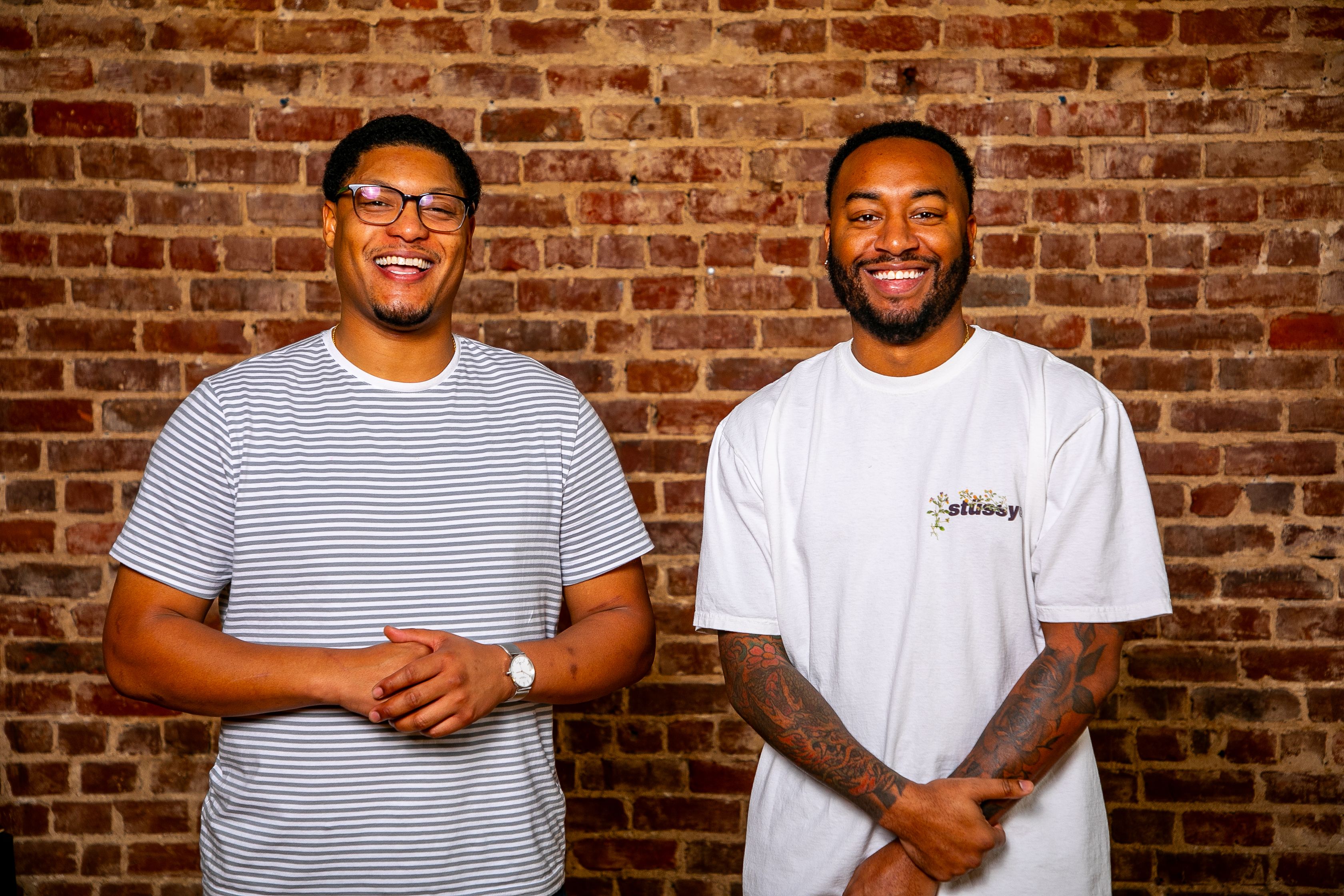 A pic of two men in front of a brick wall smiling and laughing