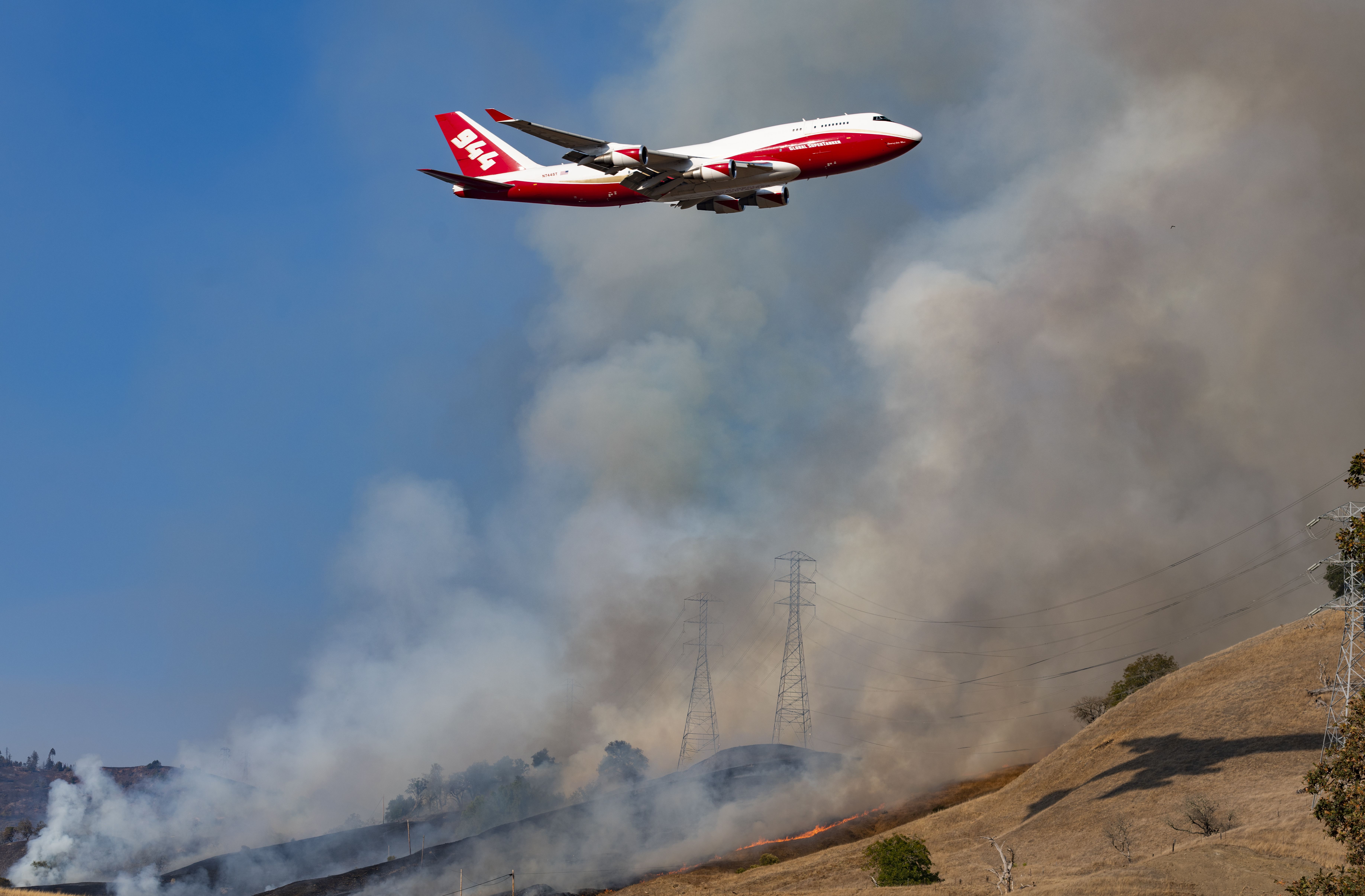 A fire fighting air tanker flies over the power transmission towers, which are engulfed in back fire set by the firefighters in an effort to control the fire in Geyserville