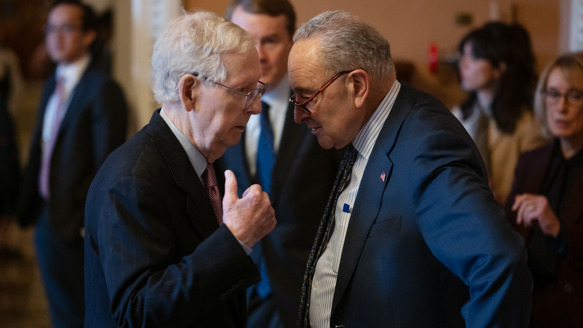 Senate Minority Leader Mitch McConnell, wearing a dark blue suit, light blue shirt, light red tie and glasses, talks to Majority Leader Chuck Schumer, wearing a blue suit, light blue shirt, blue tie and glasses.