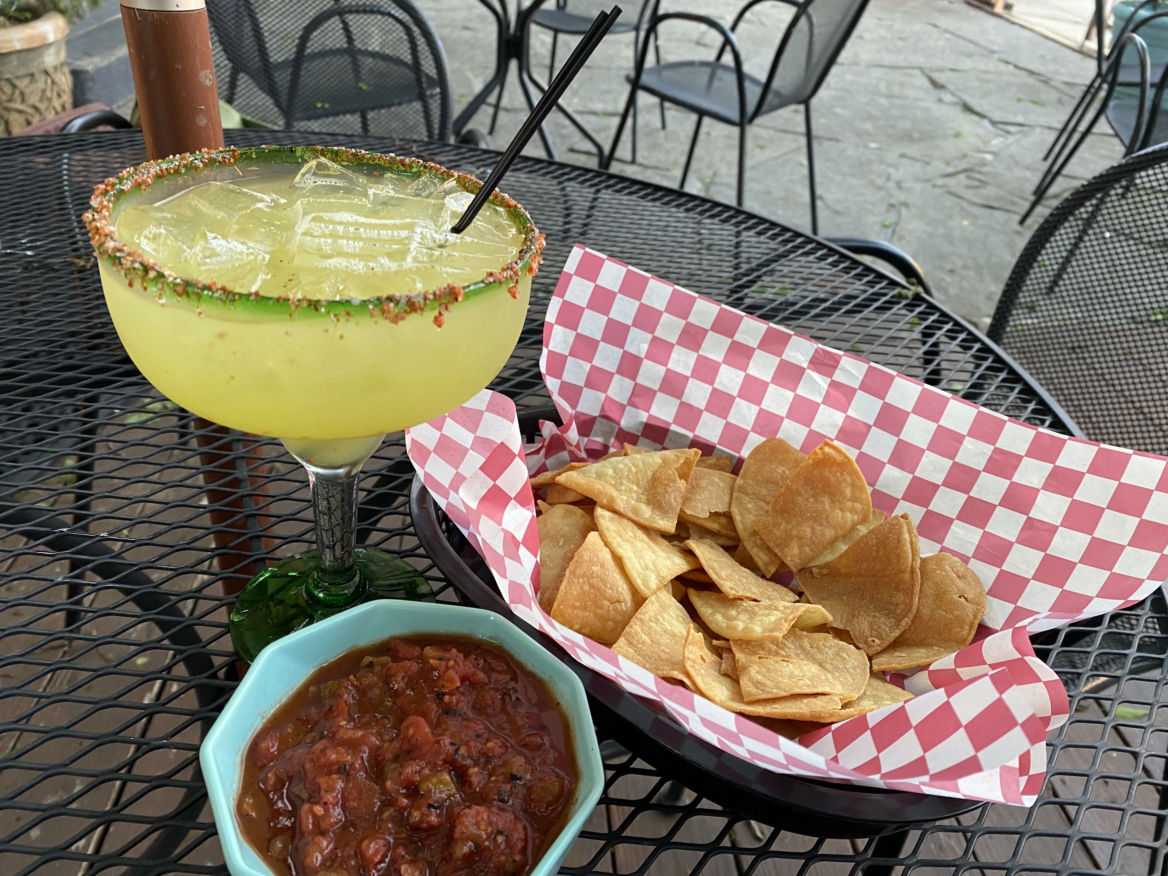 A basket of chips with a side of salsa and a margarita. 