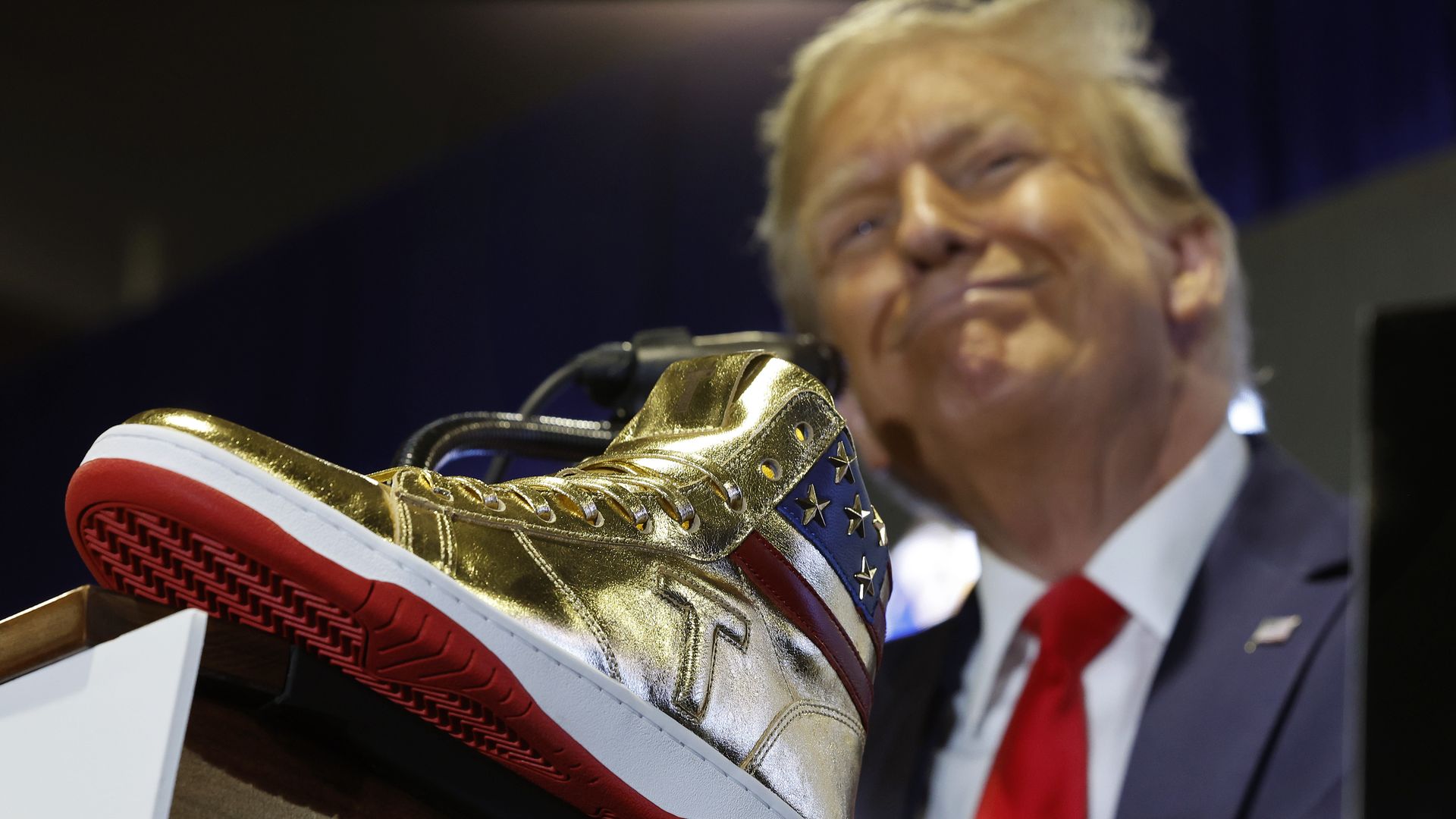 Trump above a gold sneaker with a "T" on it 