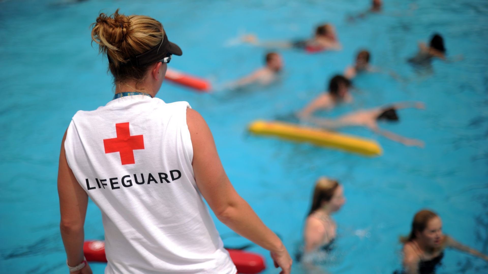 A woman in a lifeguard t-shirt watches a pool