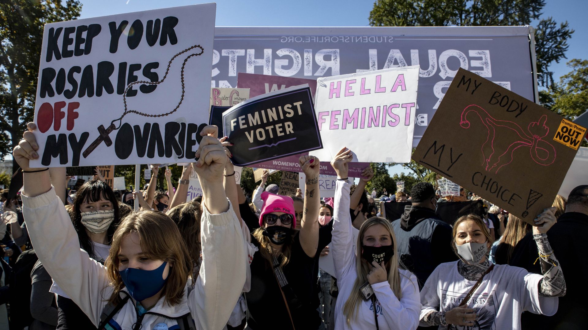 Photo of people in masks holding signs advocating for feminism and reproductive rights