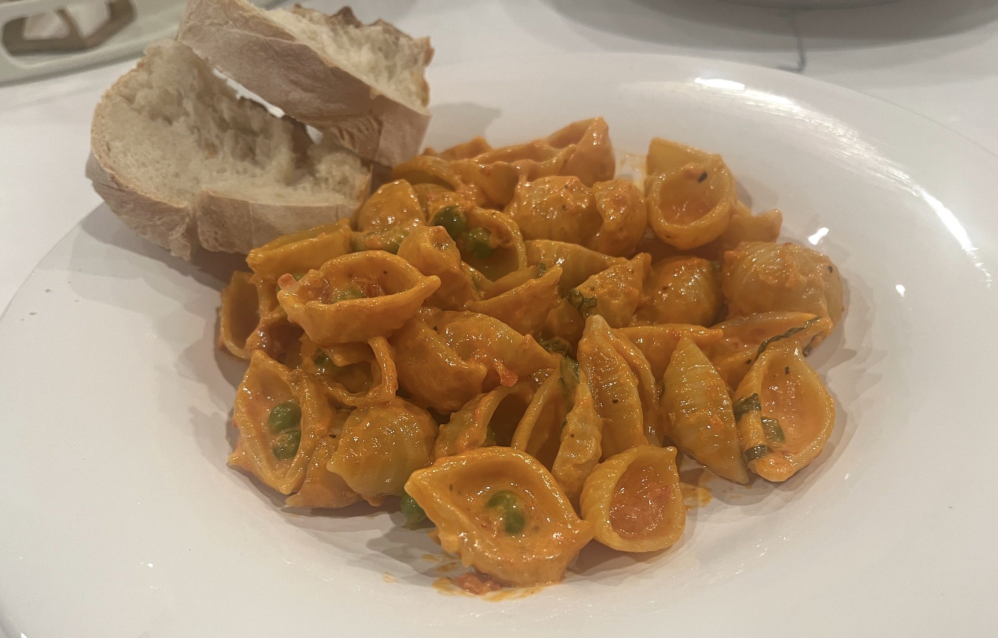 Seashell pasta with red sauce and peas with two slices of bread on the plate.