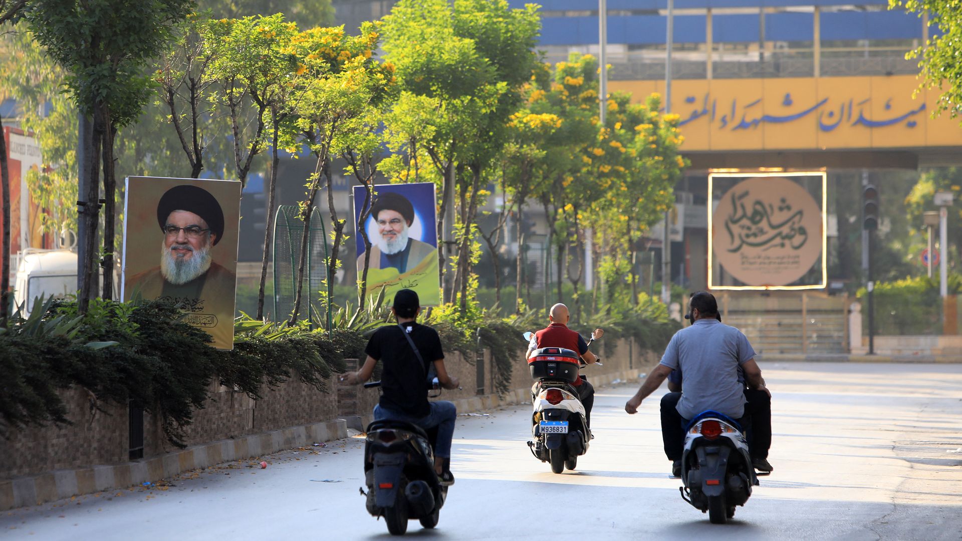 People riding motorcycles drive past portraits of slain Hezbollah leader Hassan Nasrallah in Beirut's southern suburbs on October 4, 2024. 