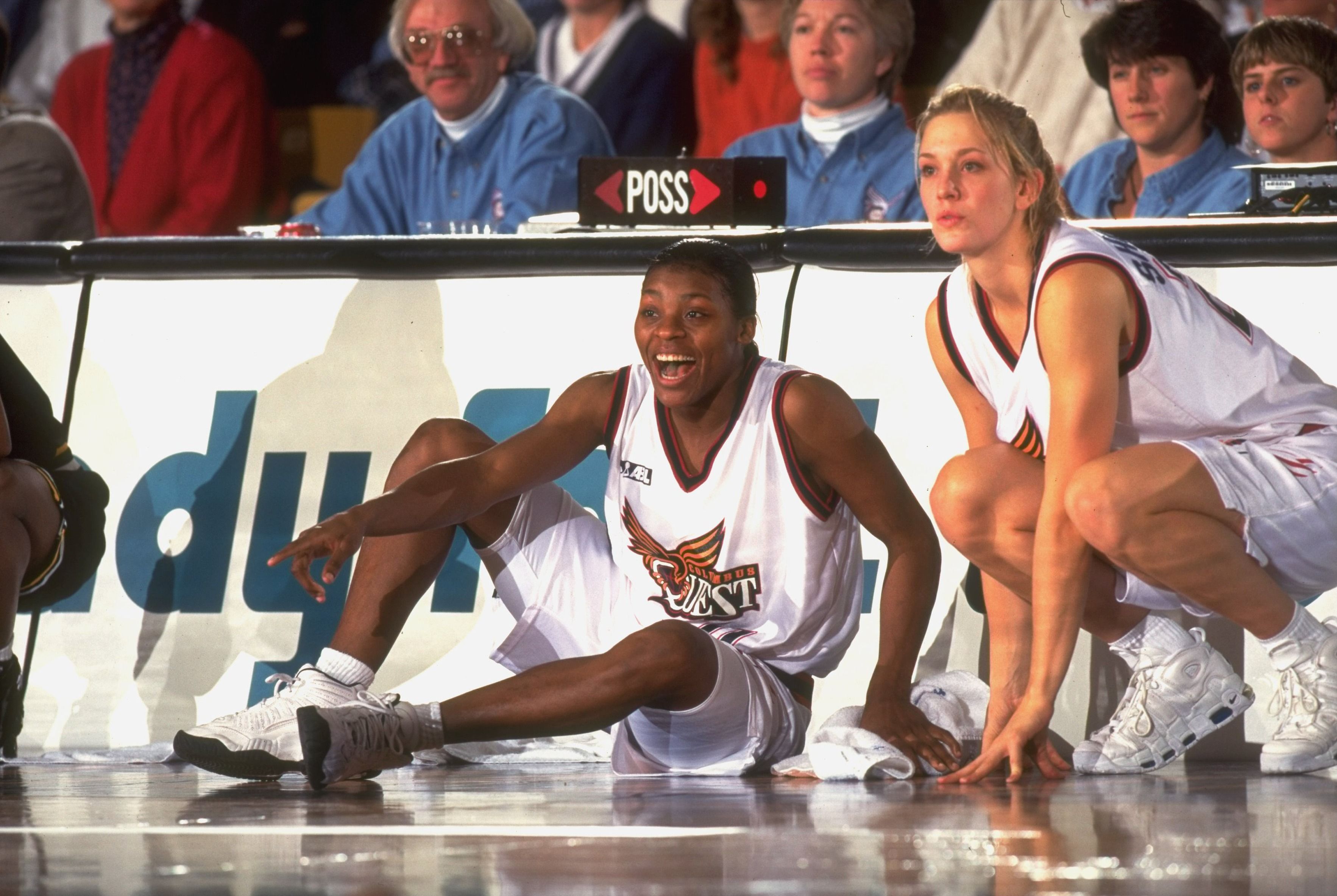 Carol Ann Shudlick and Sonja  Tate sit in front of the scorer's table during a basketball game. 