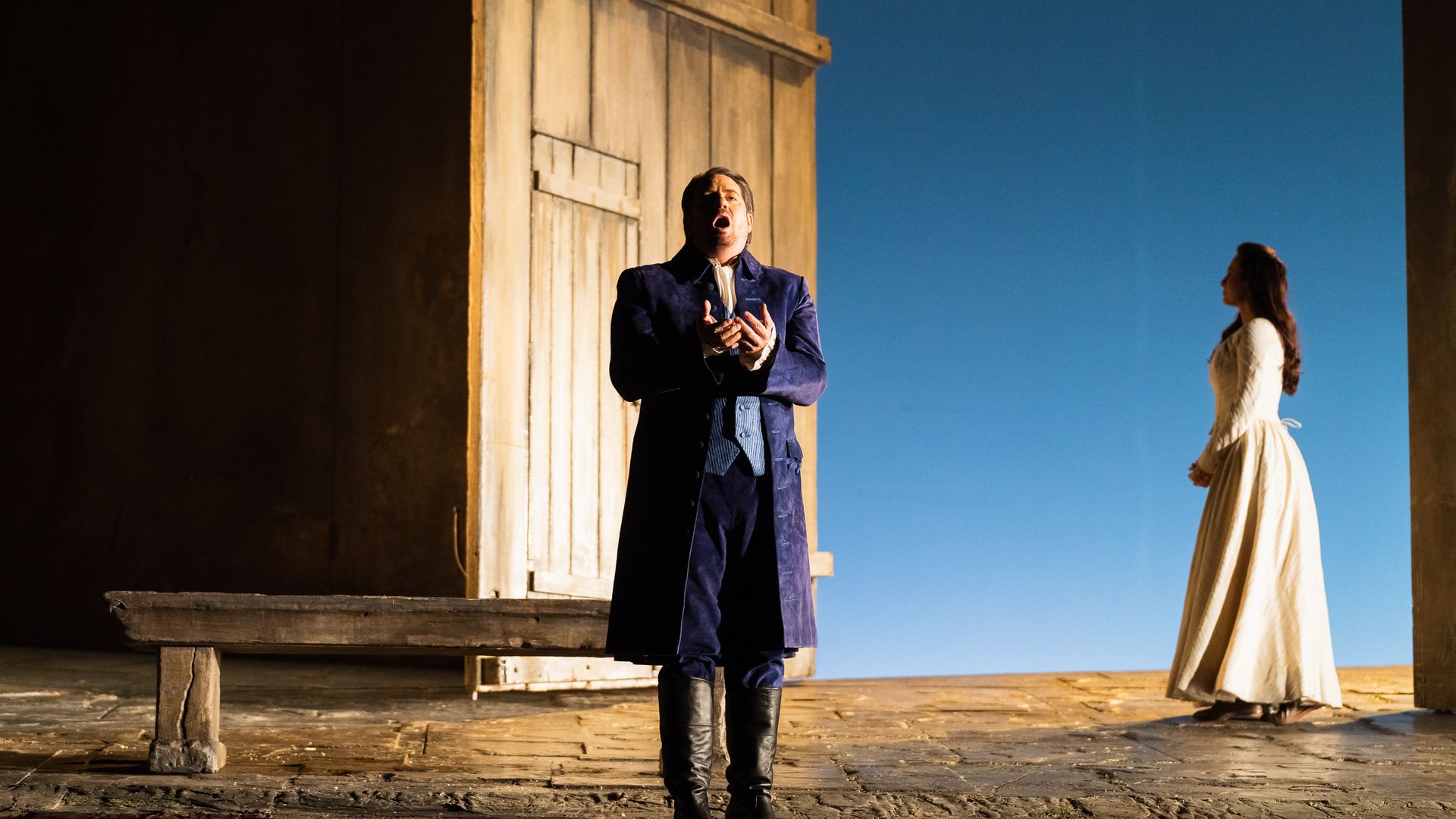 Photo of a man on stage with a large door and a woman in a white dress. 