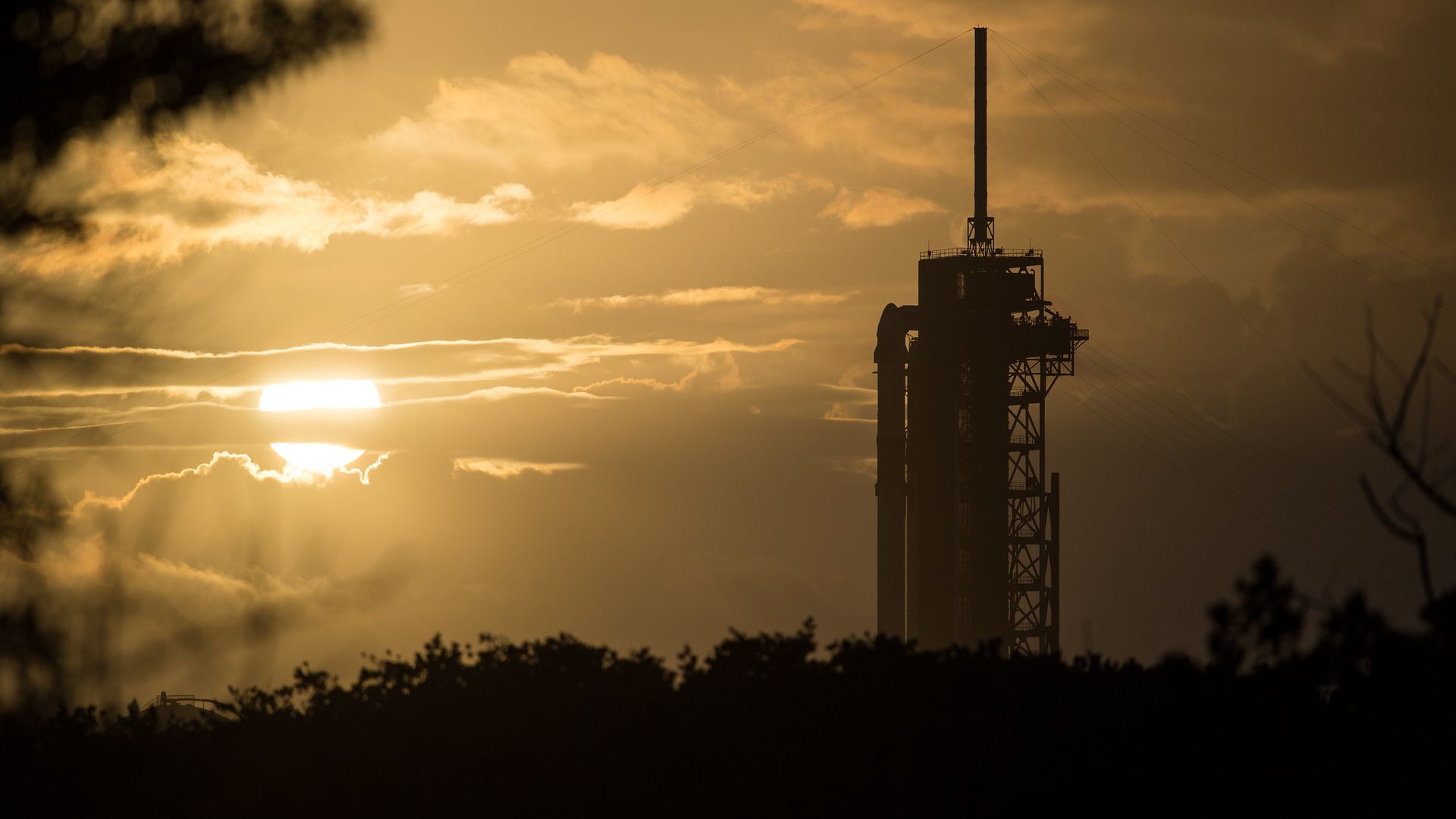 A SpaceX Falcon 9 rocket stands on a launch pad awaiting launch with the Sun rising beautifully in front of it