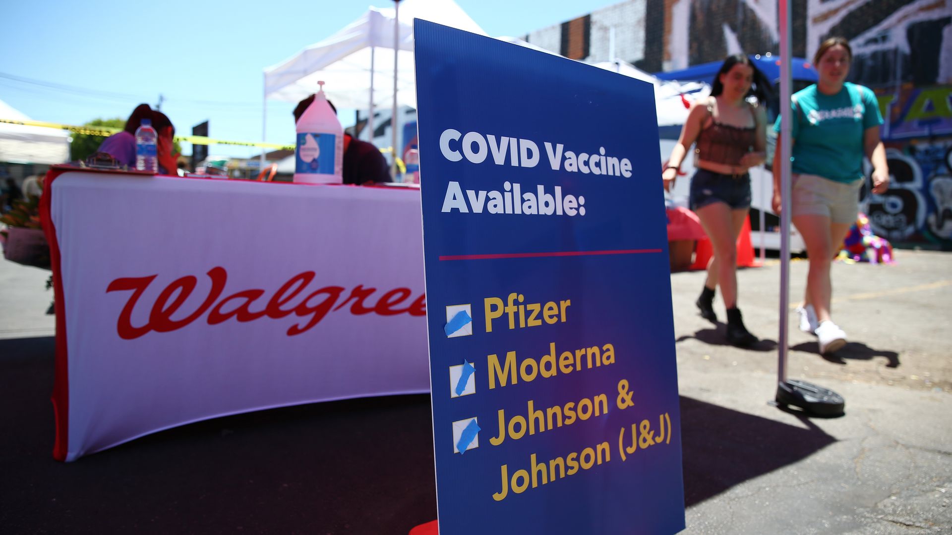 A blue sign advertising COVID vaccines in front of a Walgreens booth.