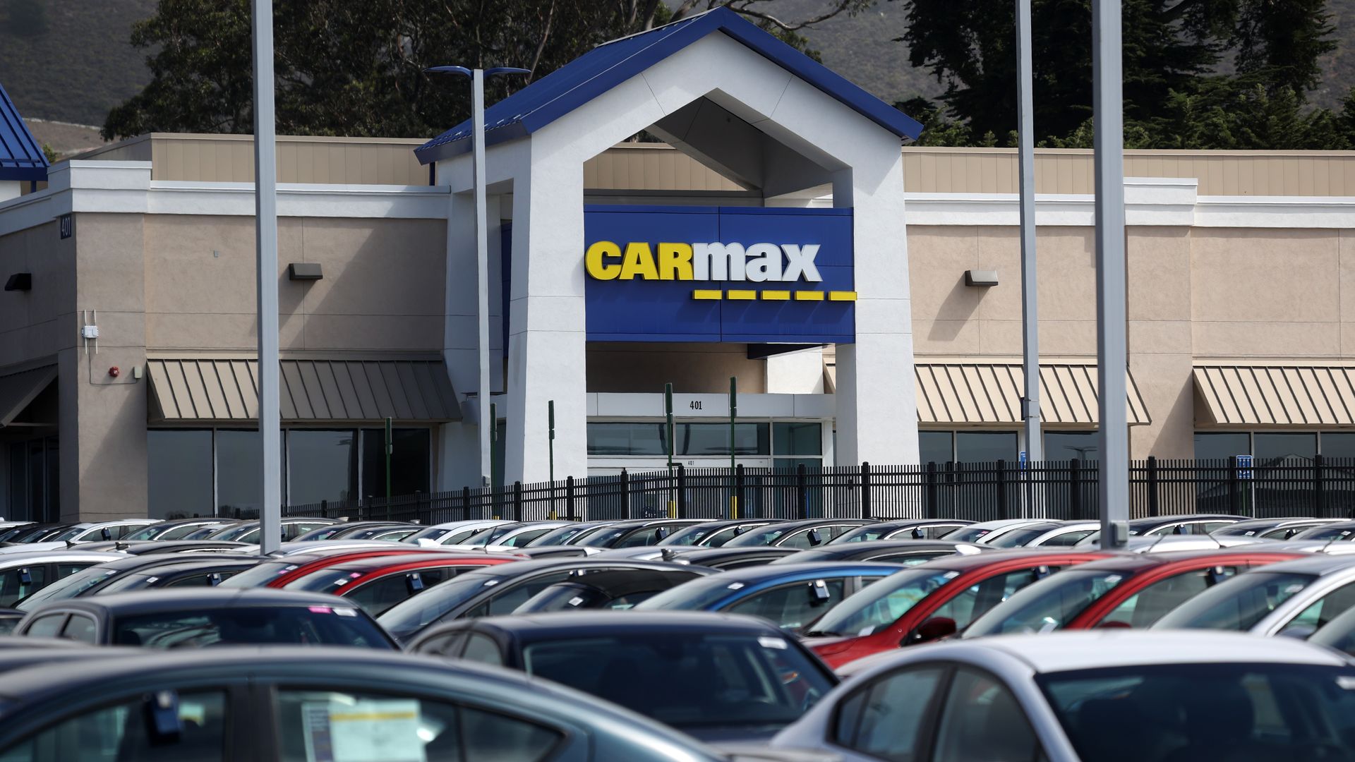 CarMax dealership building with a blue and white sign and a parking lot full of various colored cars.