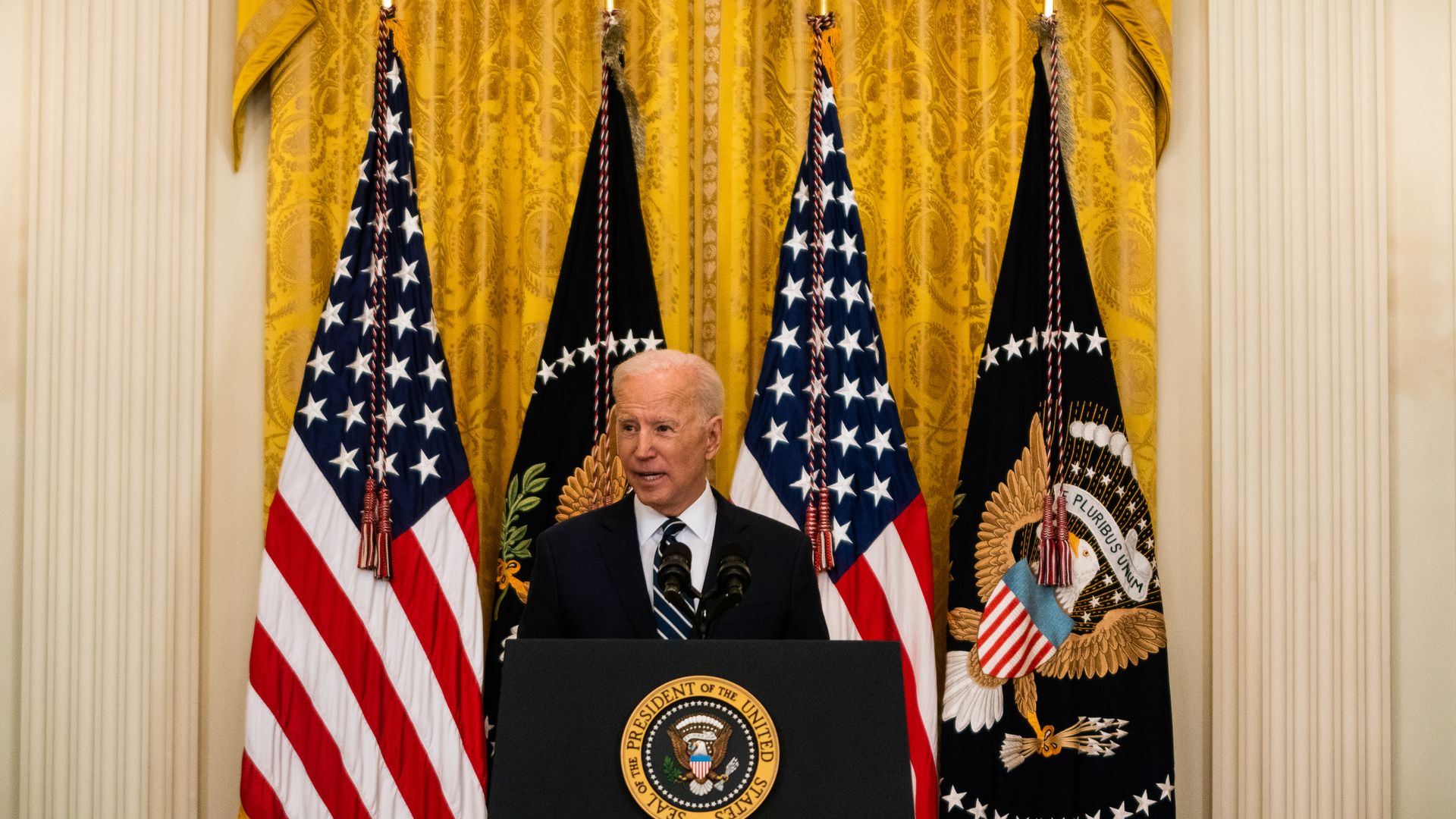 Joe Biden speaking from behind a podium with American flags behind him
