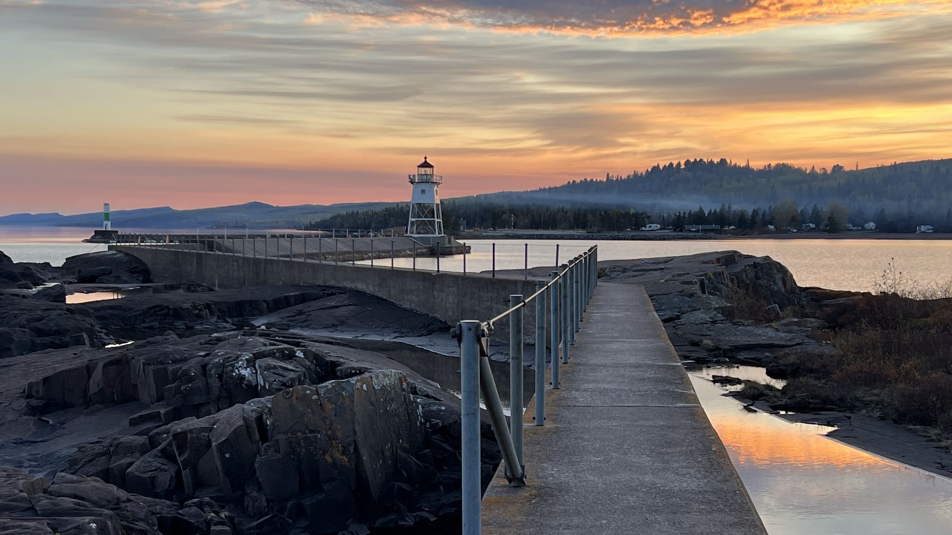 A pier and a lighthouse at sunset near water