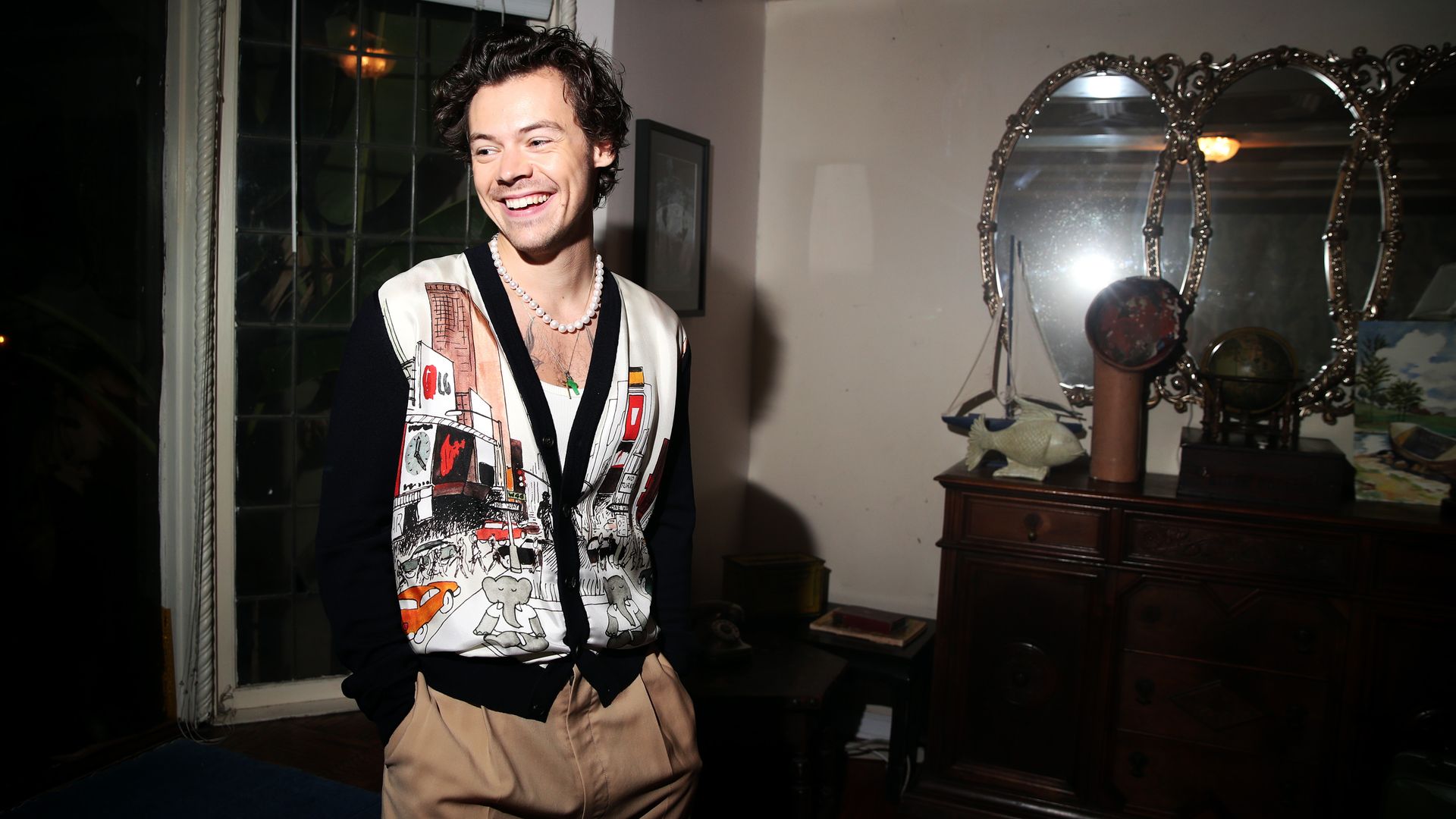 Harry Styles smiles in a sweater and khaki pants.