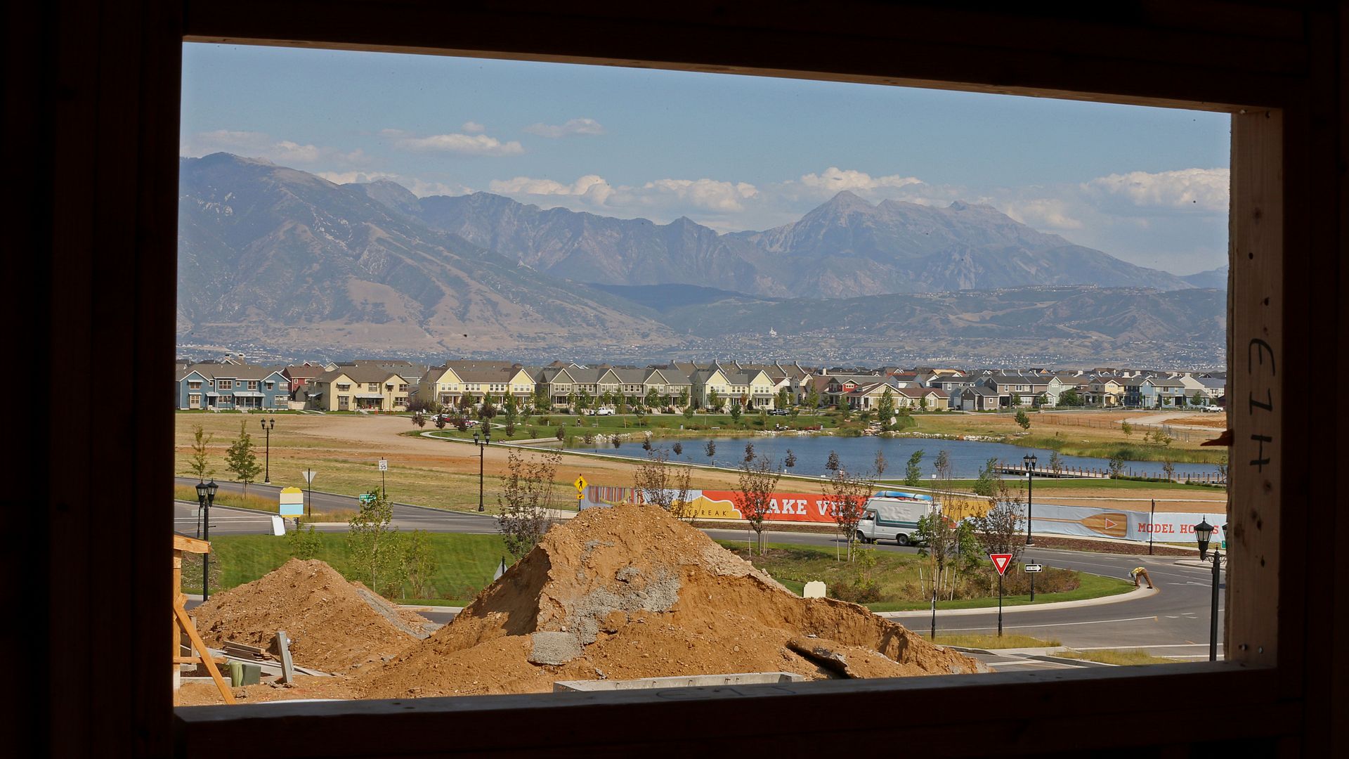 A city with construction dirt in the foreground, viewed through a window of an under-construction house. 