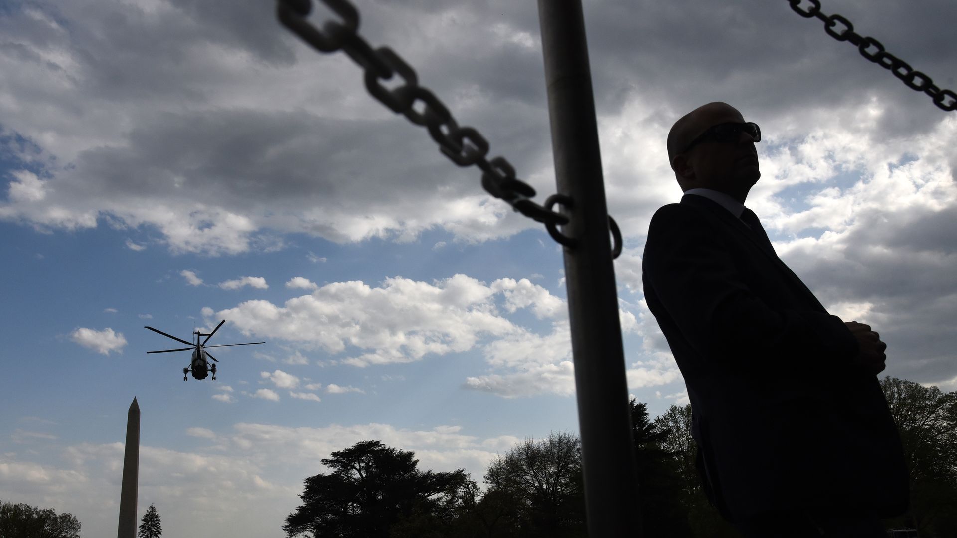 A Secret Service agent stands as Marine One flies away behind him.