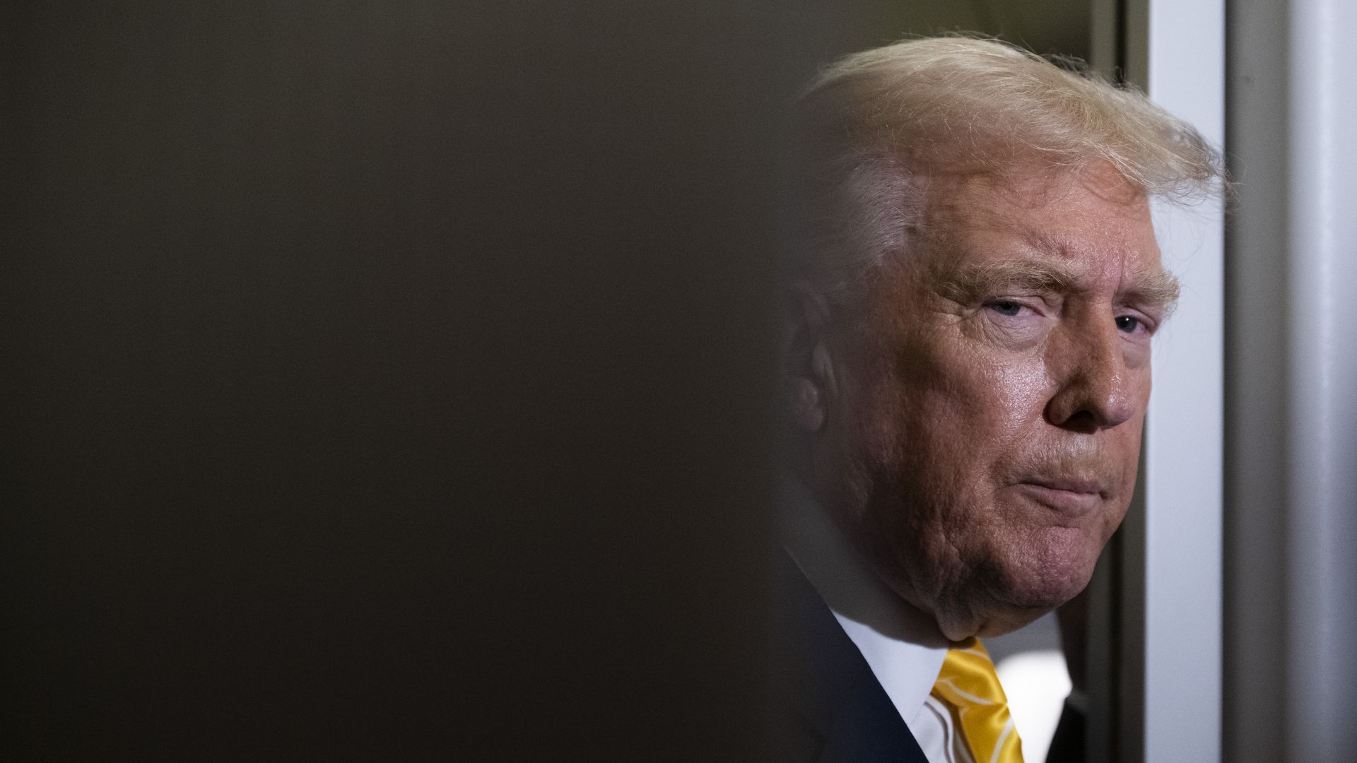 President Trump, in a white shirt and gold tie, seen looking through a doorway.