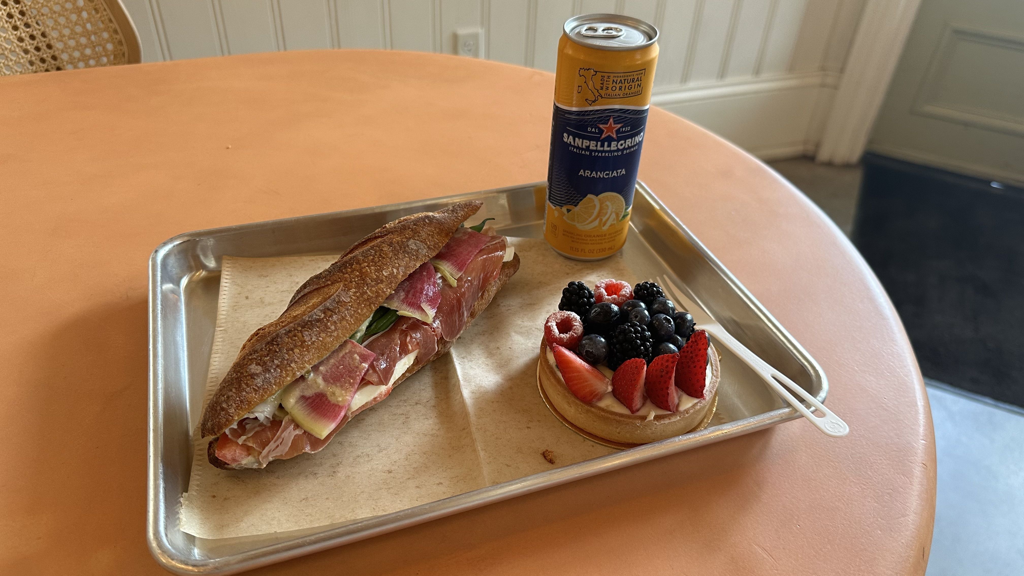 A baguette sandwich, a fruit tart and a Pellegrino are served on a metal tray.