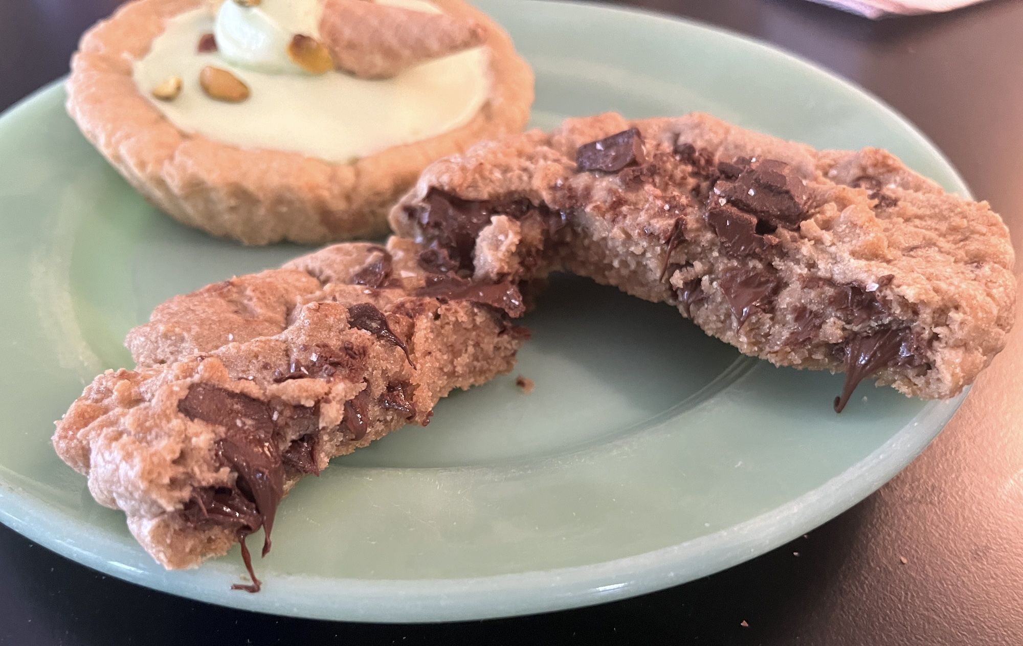 Chocolate chip cookie with sea salt cut in half and sitting on green plate.