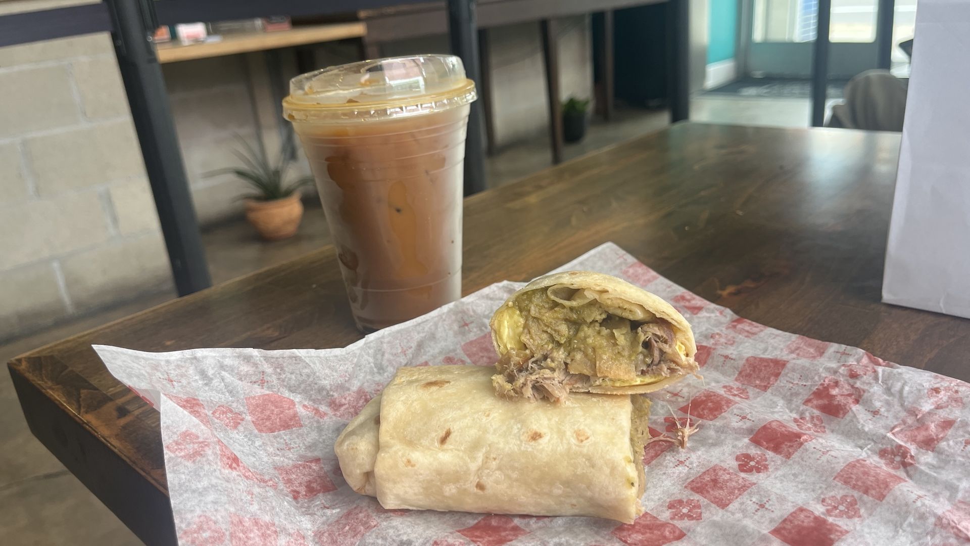A chilaquiles breakfast burrito cut in half to show the inside and a cold brew.