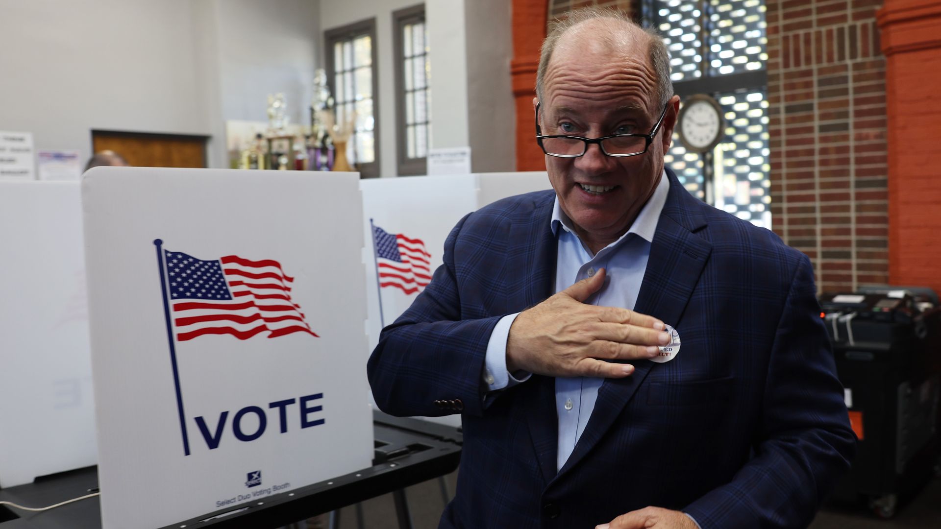Mike Duggan at a voting booth affixing a sticker is his suit's lapel