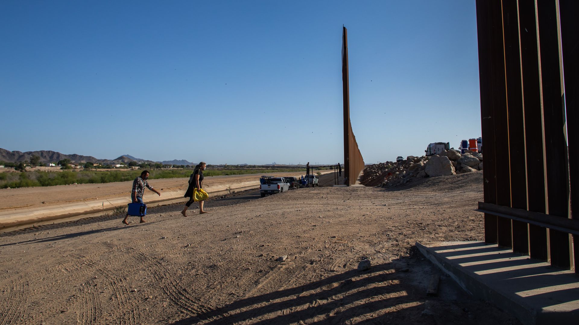 Photo of two people crossing the U.S.-Mexico border under a sunny day