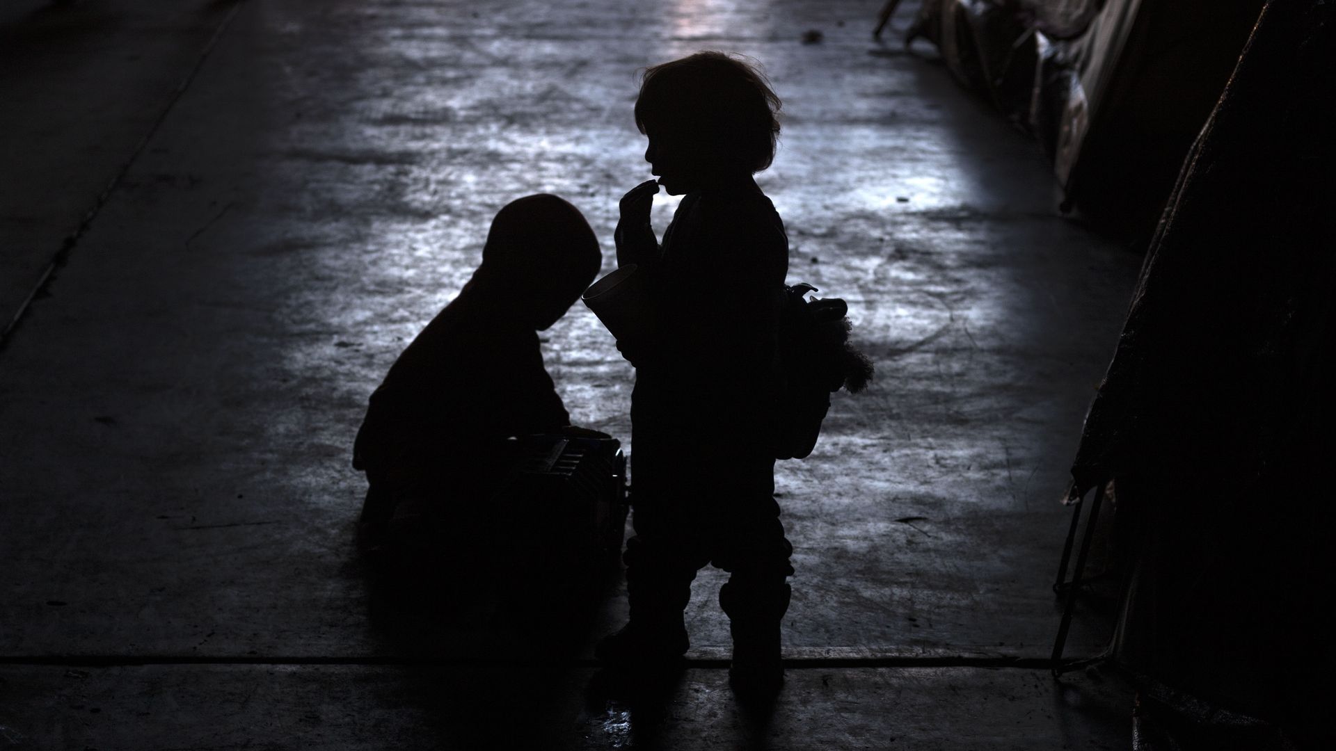 Silhouettes of two young, migrant children at night by the border