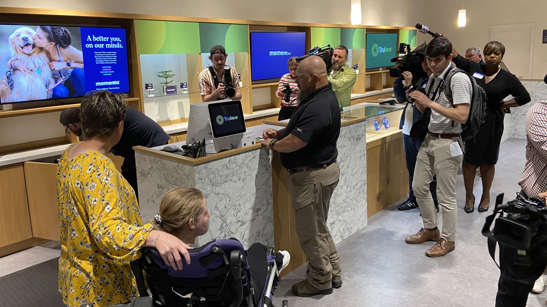 A family with a daughter who uses a wheelchair purchases medical cannabis while news crews take photos and video