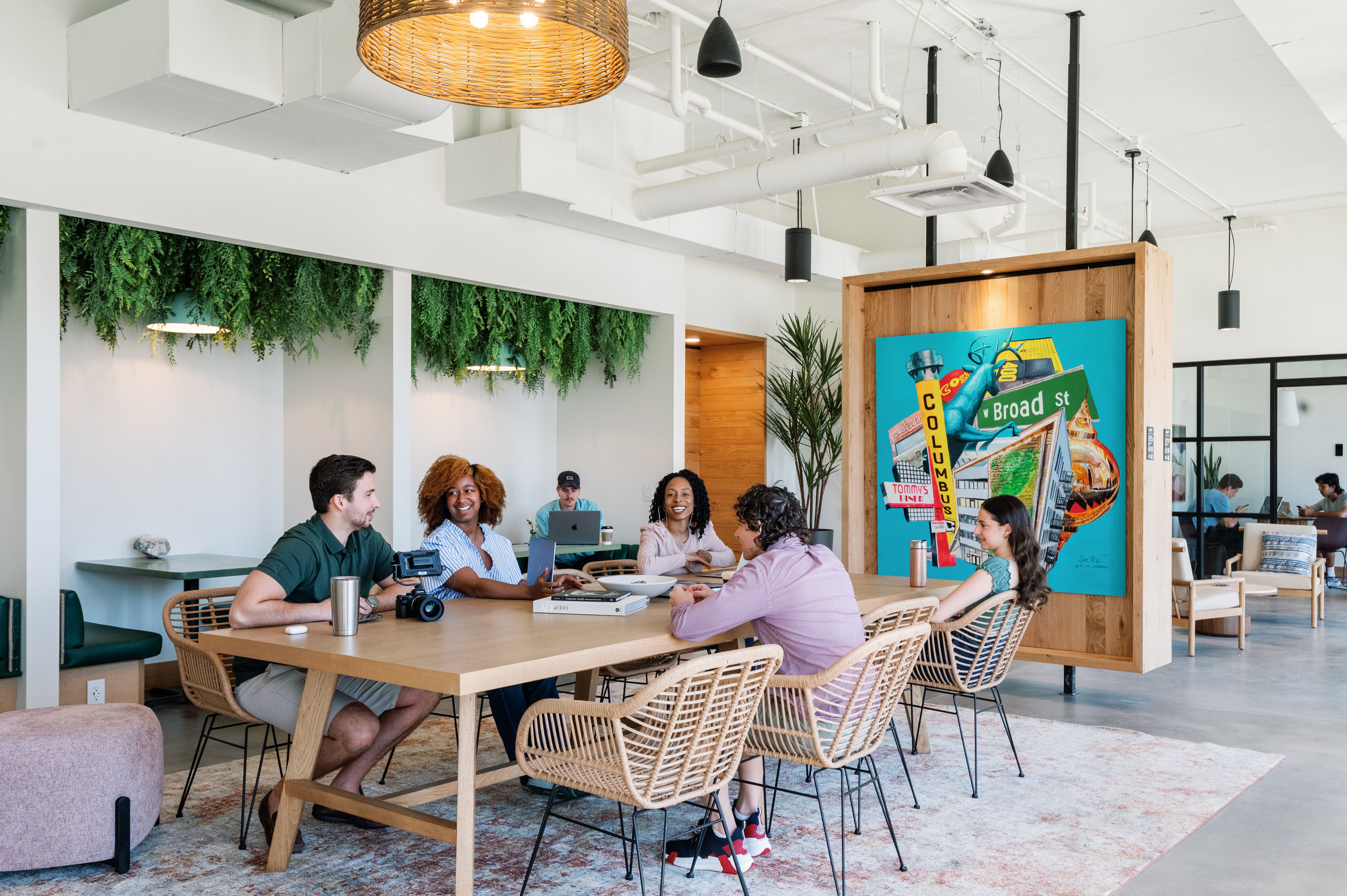 A coworking space in a Gravity apartment building, with tenants gathered at large tables near a Columbus-themed mural