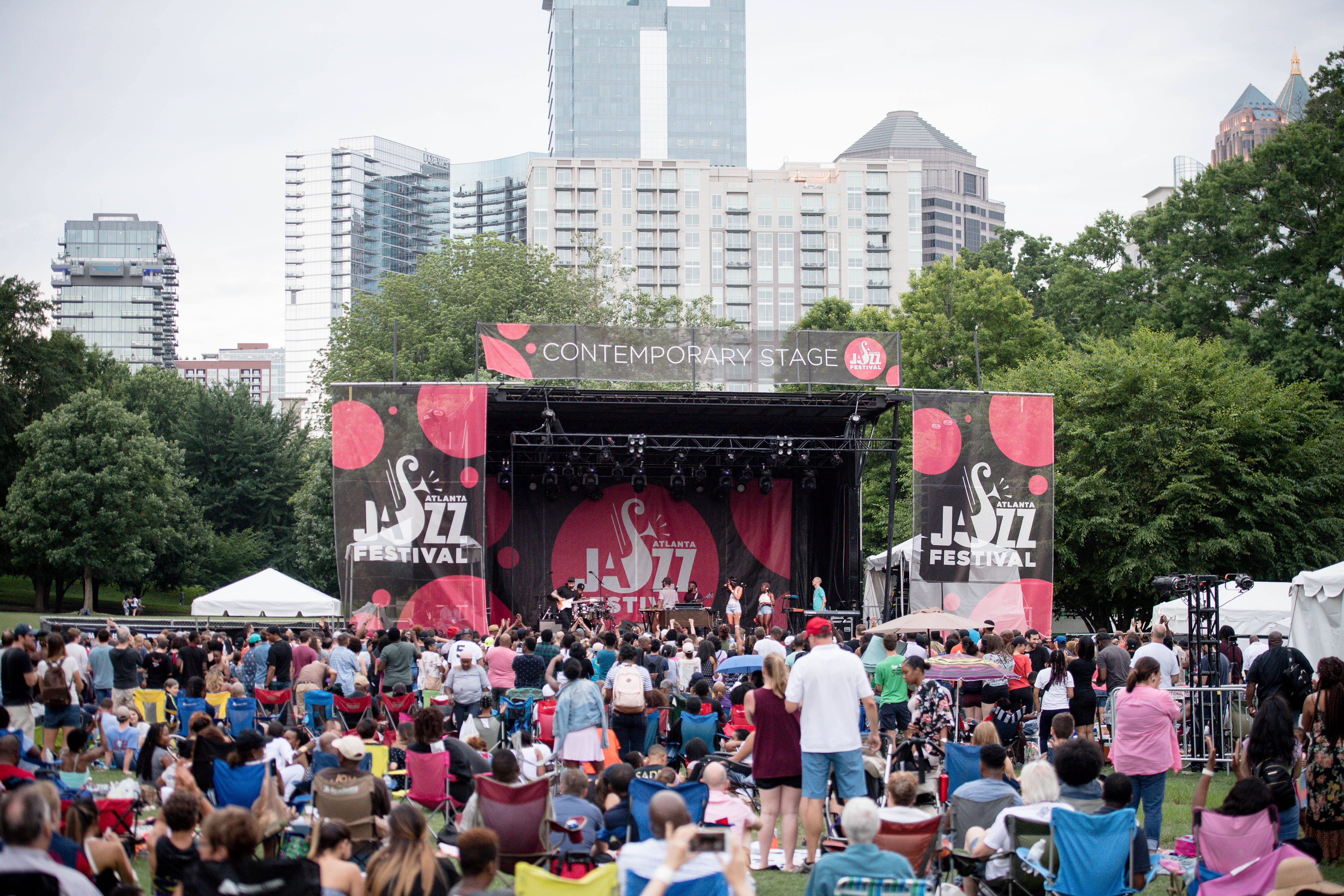 People attend an outdoor jazz festival in a verdant park with the Atlanta skyline in the background