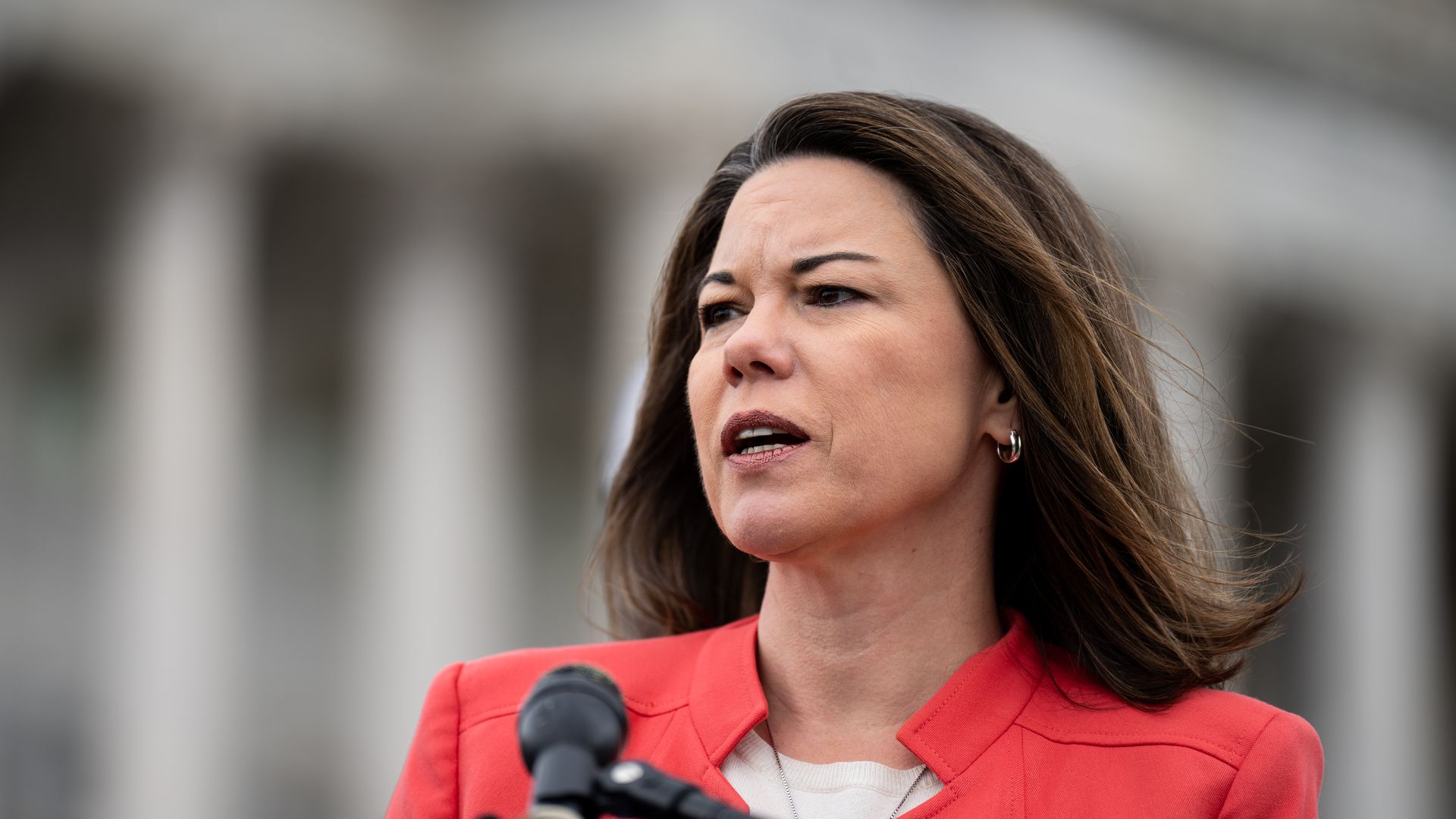 U.S. Rep. Angie Craig speaking at a microphone in a pink blazer