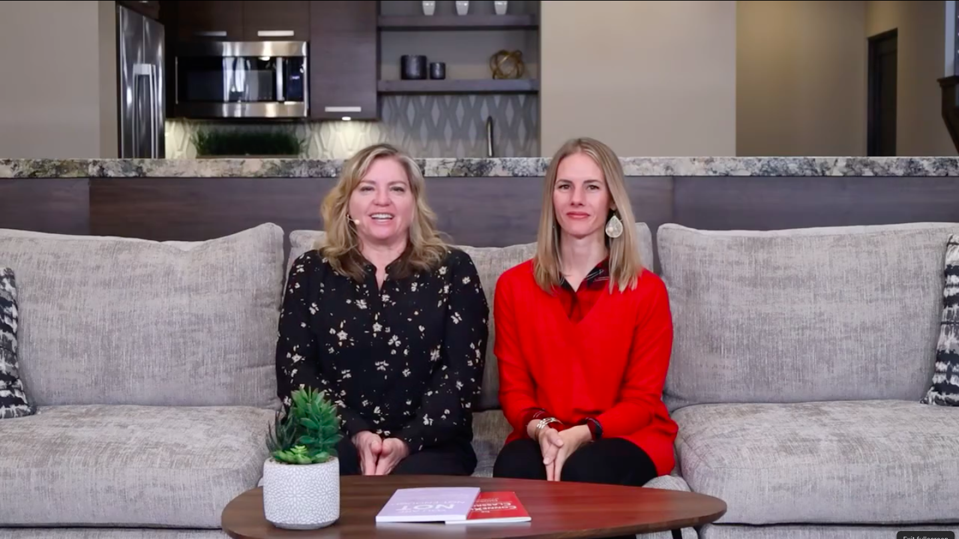 Two women sitting on a gray couch.