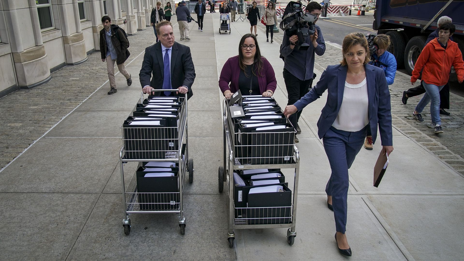 Two people roll shopping carts of binders down a sidewalk