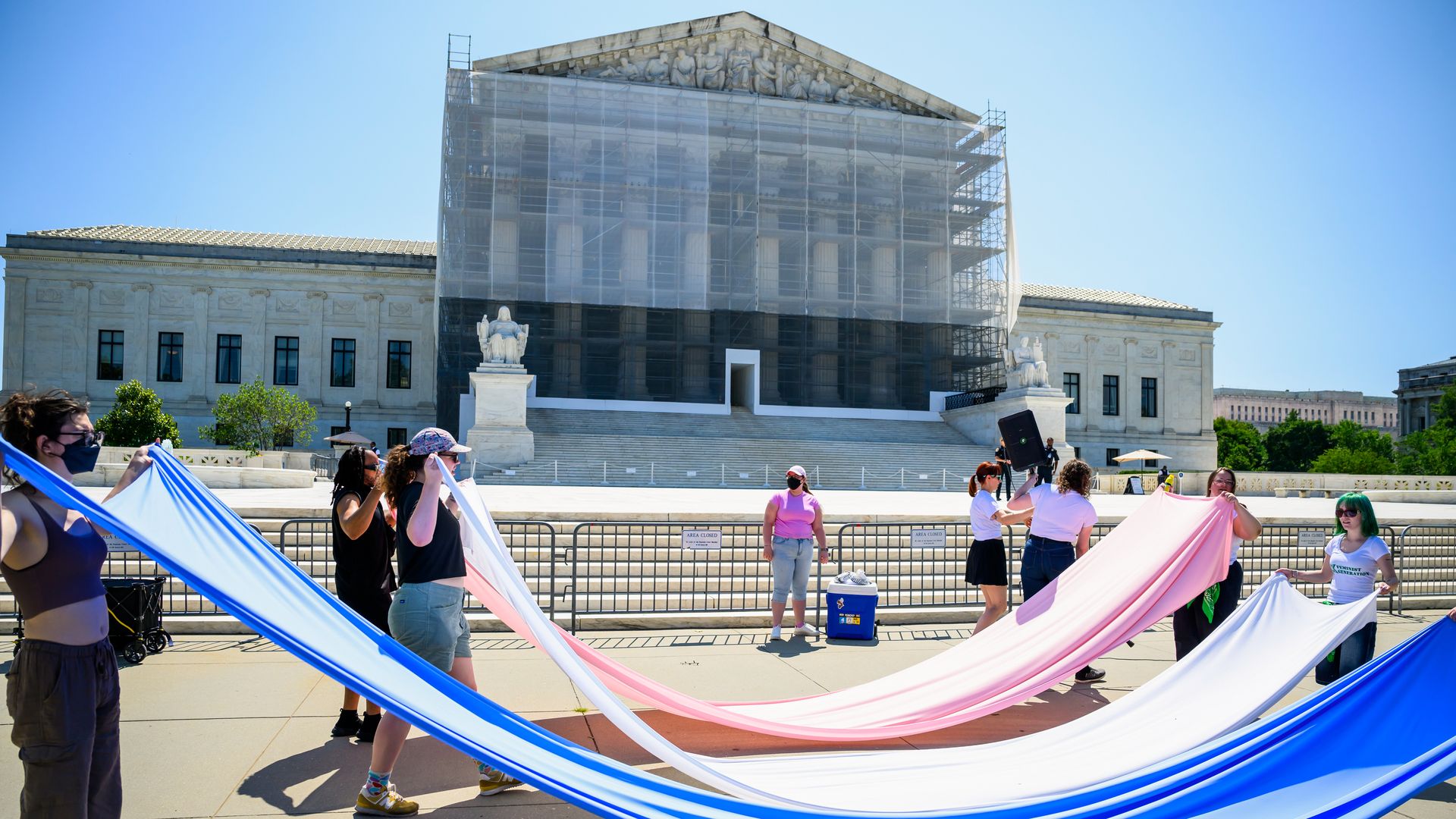 A group of people hold pink, white and blue sheets to make a transgender flag in front of the Supreme Court.
