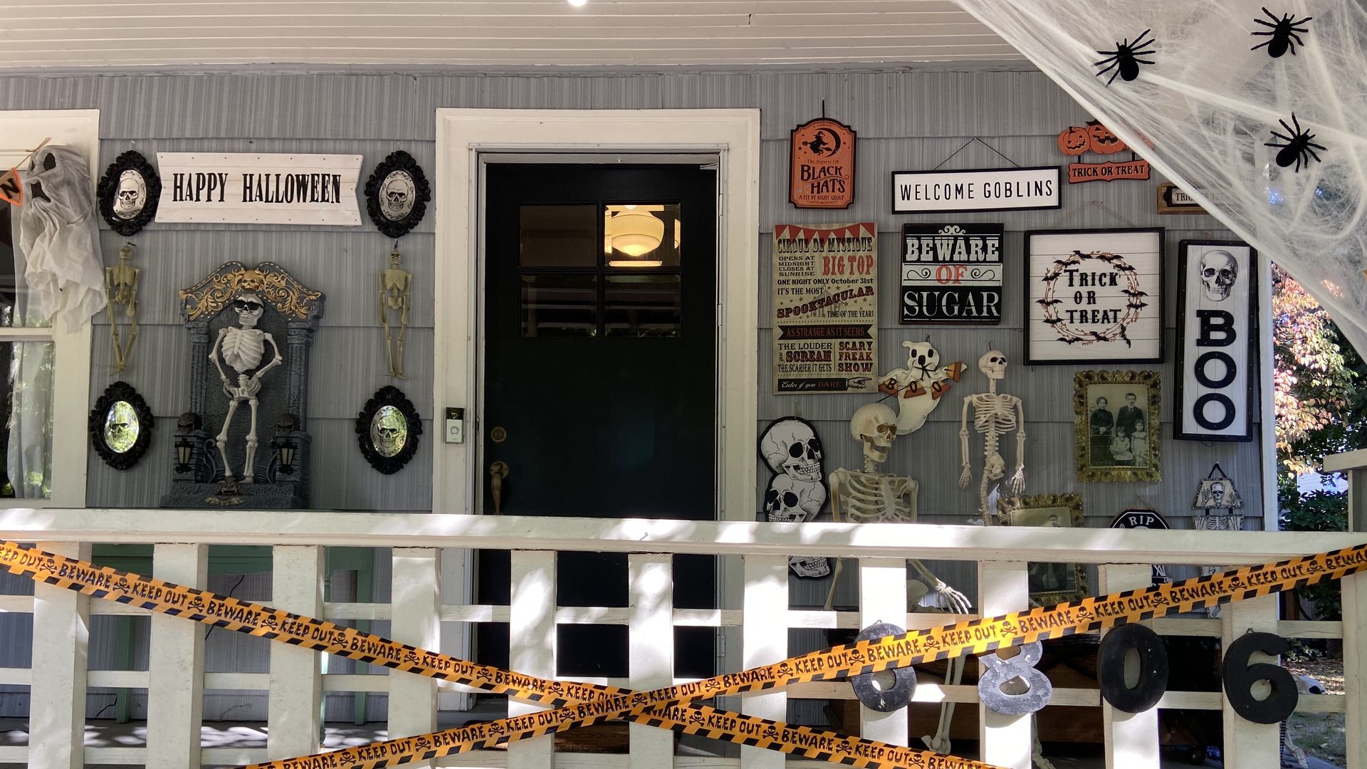 The front of a house decorated with Halloween decorations including skeletons, signs that say boo and orange caution tape.