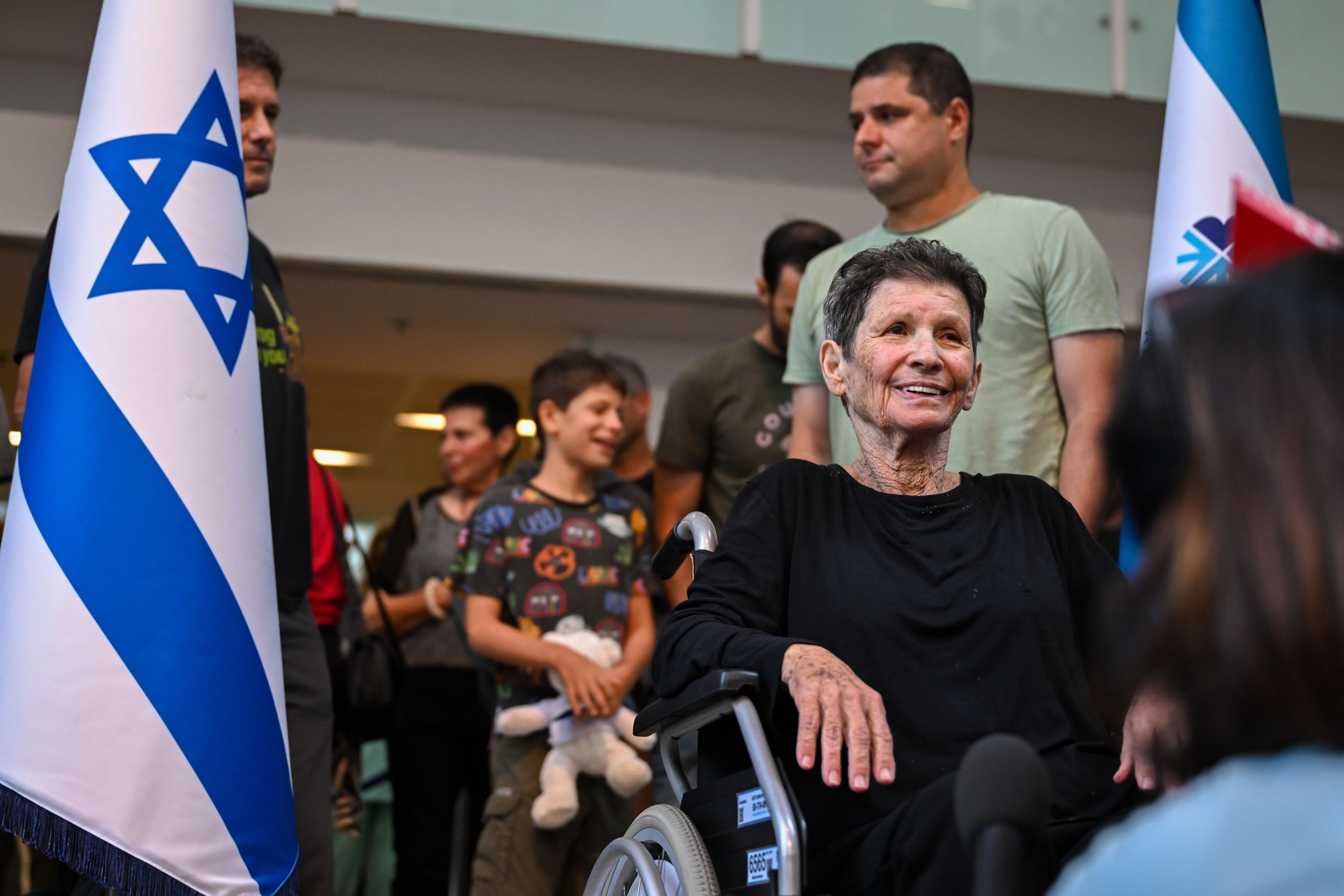 A woman in a wheelchair smiles up at unseen people in the foreground. 