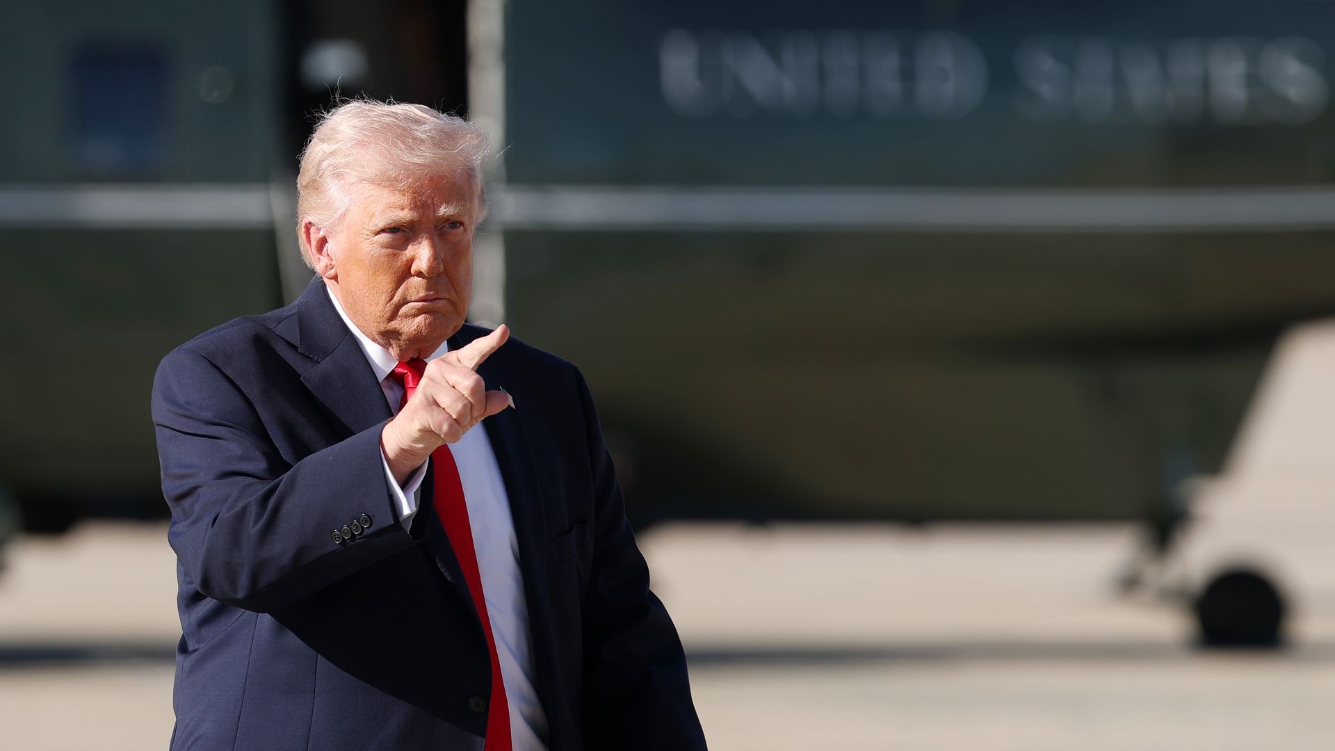 Donald Trump points with Marine One in the background.