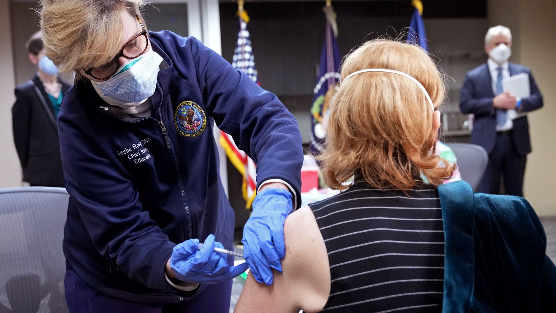 Photo of a masked medical worker giving a vaccine jab to a person sitting down