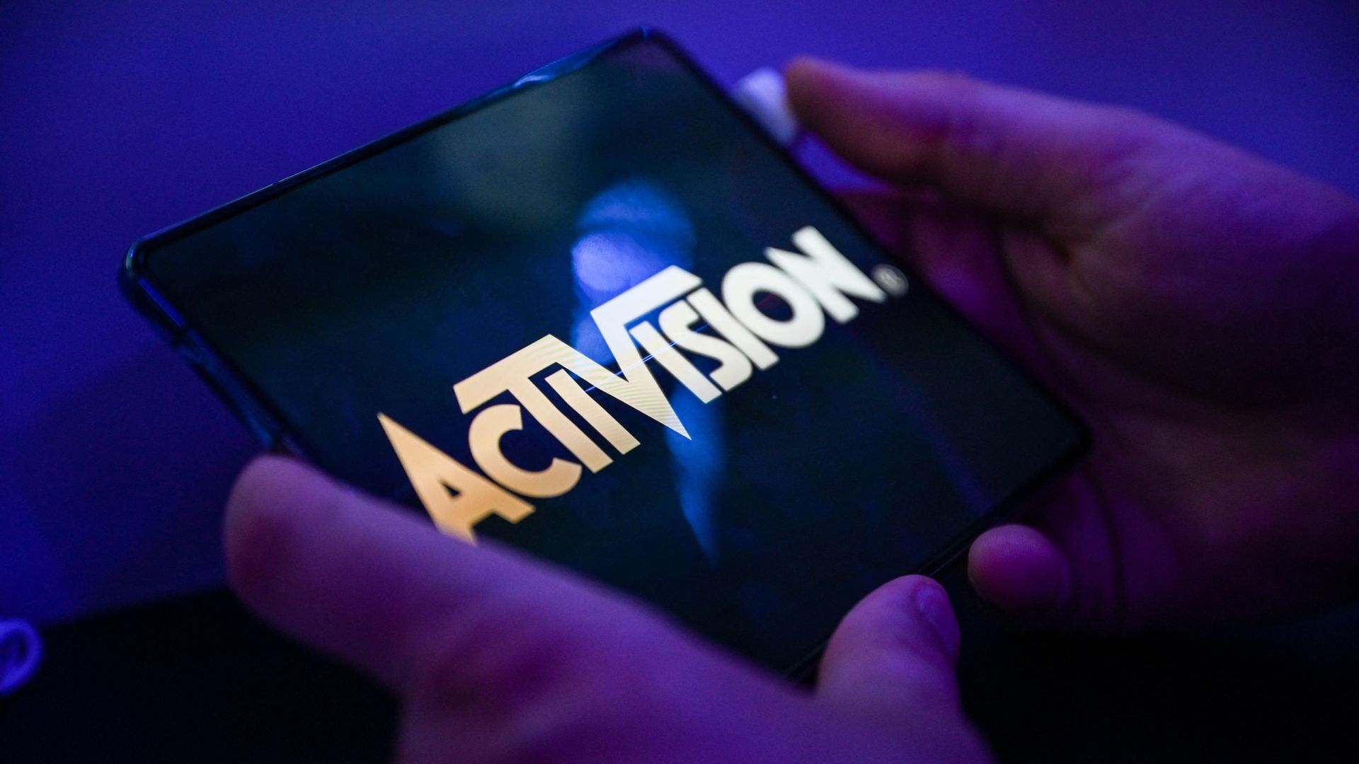 Close-up photo of a person's hands as they hold a cell phone that is displaying an Activision logo