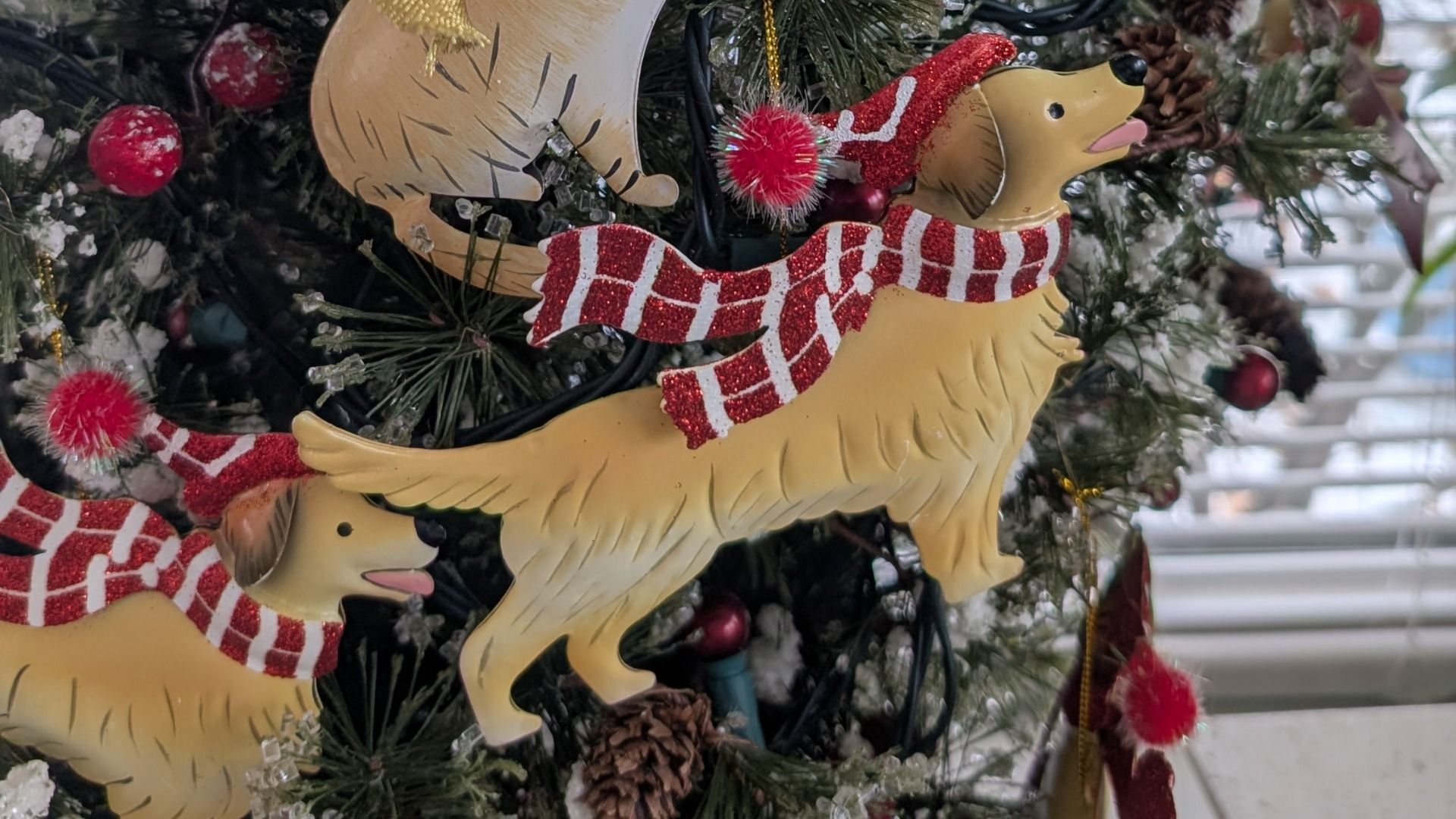 Christmas tree decorated with ornaments of yellow dogs wearing red and white striped scarves and Santa hats, surrounded by pine cones and red berries.