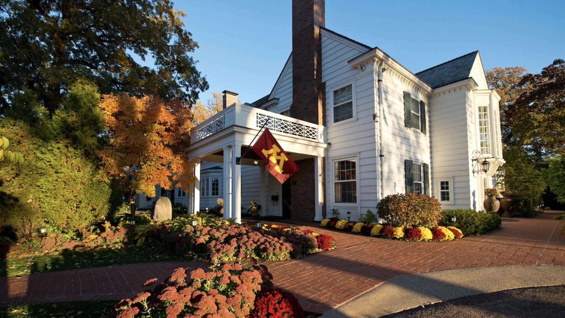 large white house with maroon and gold flowers and a gold and maroon U of M flag