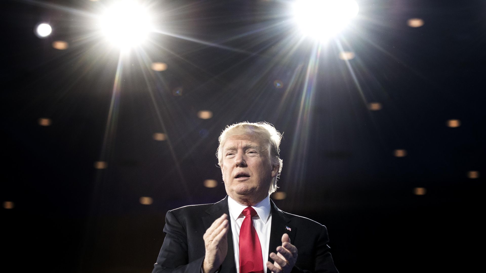 In this image, President Trump stands on stage behind two bright lights.