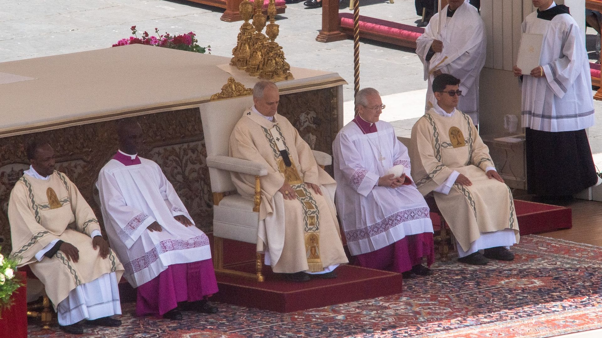 Pope Leo XIV sits on a chair surrounded by four other clergy men.