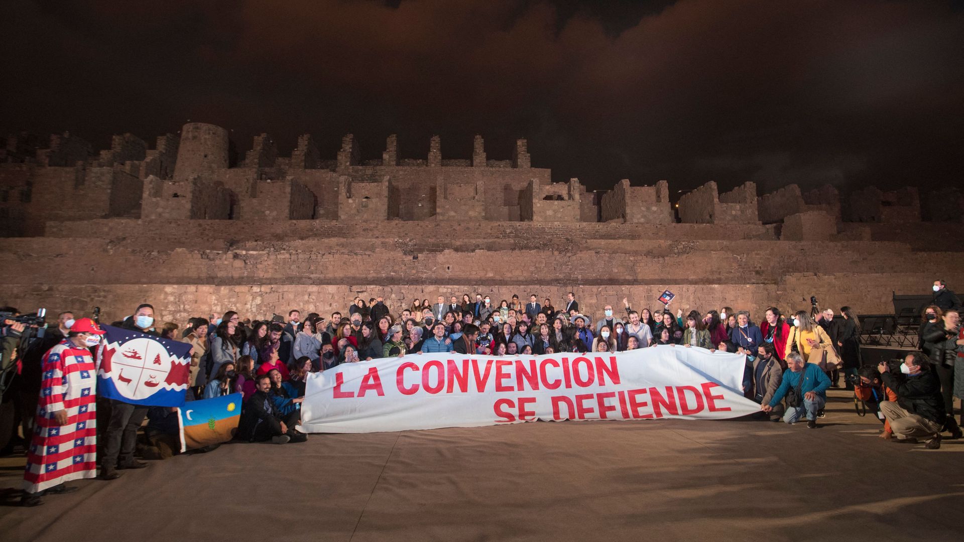 A large group of people writing Chile's new constitution pose behind a large banner that says "we defend the convention" after finishing a draft on Tuesday 
