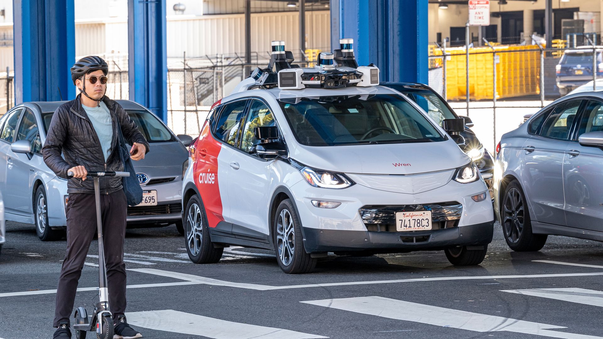 Image of a Cruise robotaxi on a busy street in San Francisco, as a person on a scooter rides by. 