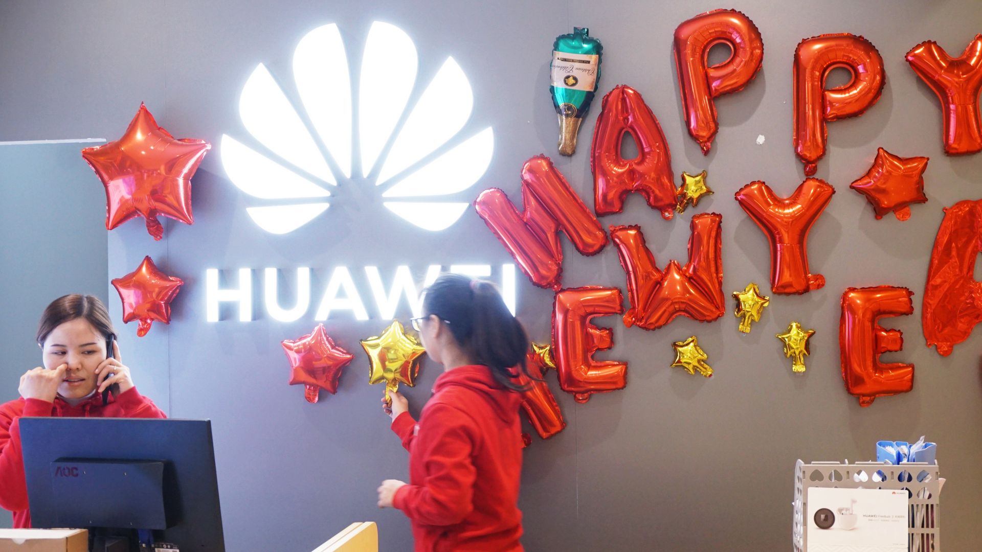 In this image, two women hang up Happy New Year balloons while working at a Huawei store