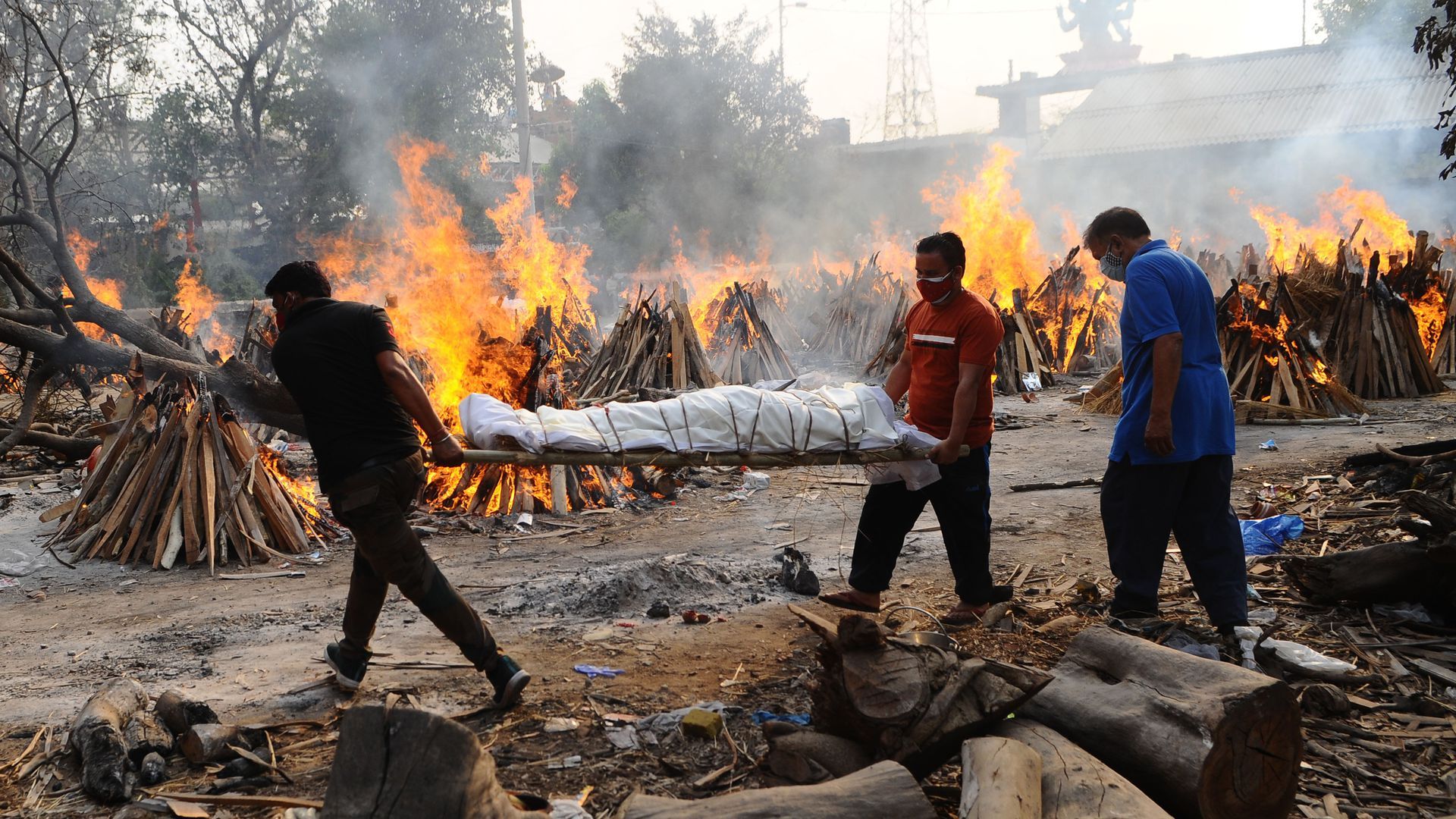 Picture of two Indian men carrying a body on a wooden plank, the body is wrapped with sheets