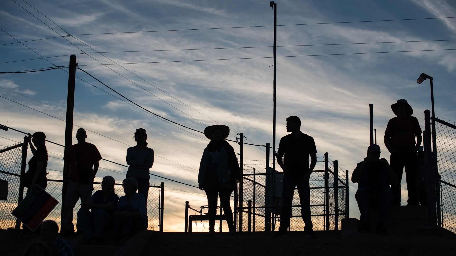 Silouettes of several people standing on a roof with a sunset in the background