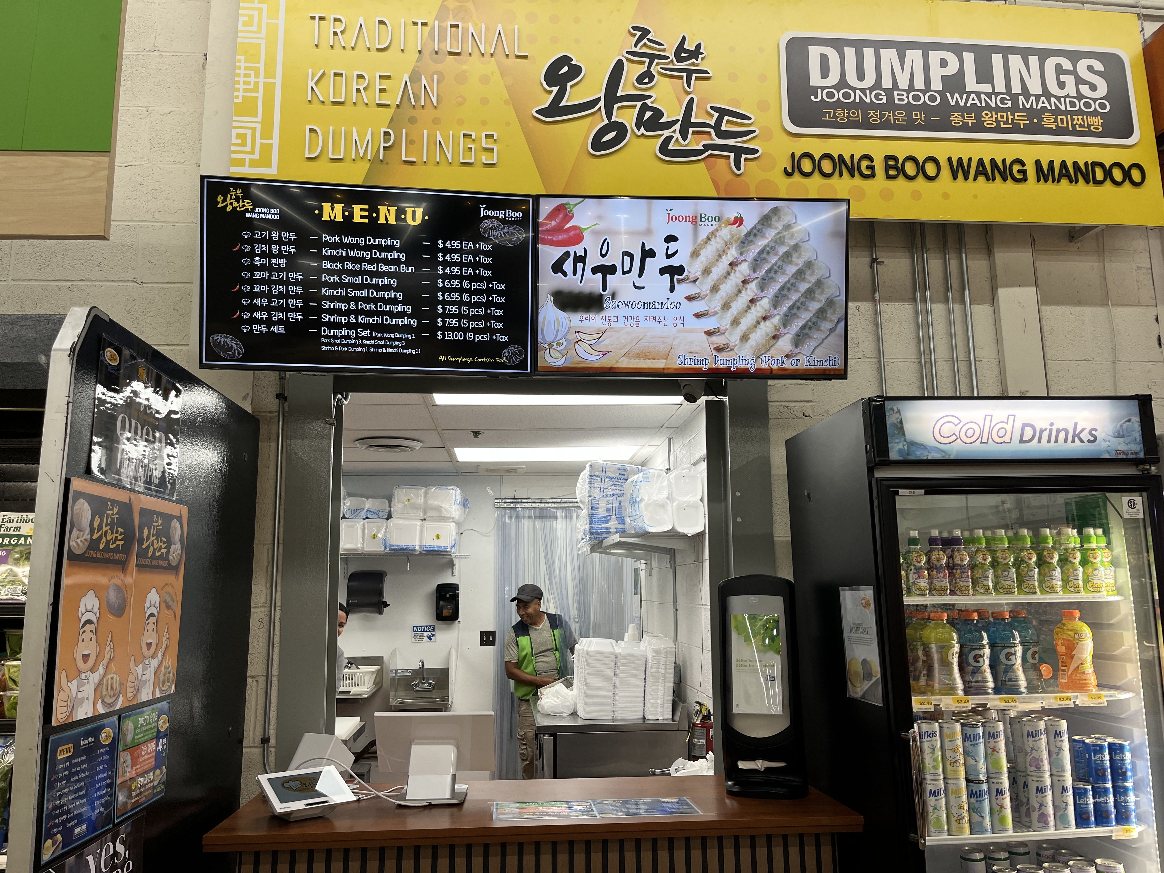 Traditional Korean dumplings food stall named Joong Boo Wang Mandoo with yellow signage, digital menu board, workers inside, and a refrigerator labeled "Cold Drinks" with assorted beverages.