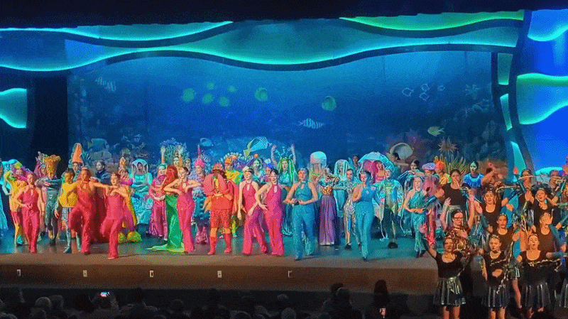A stage production of "The Little Mermaid," with an actor playing Ariel suspended over a cast of fish.