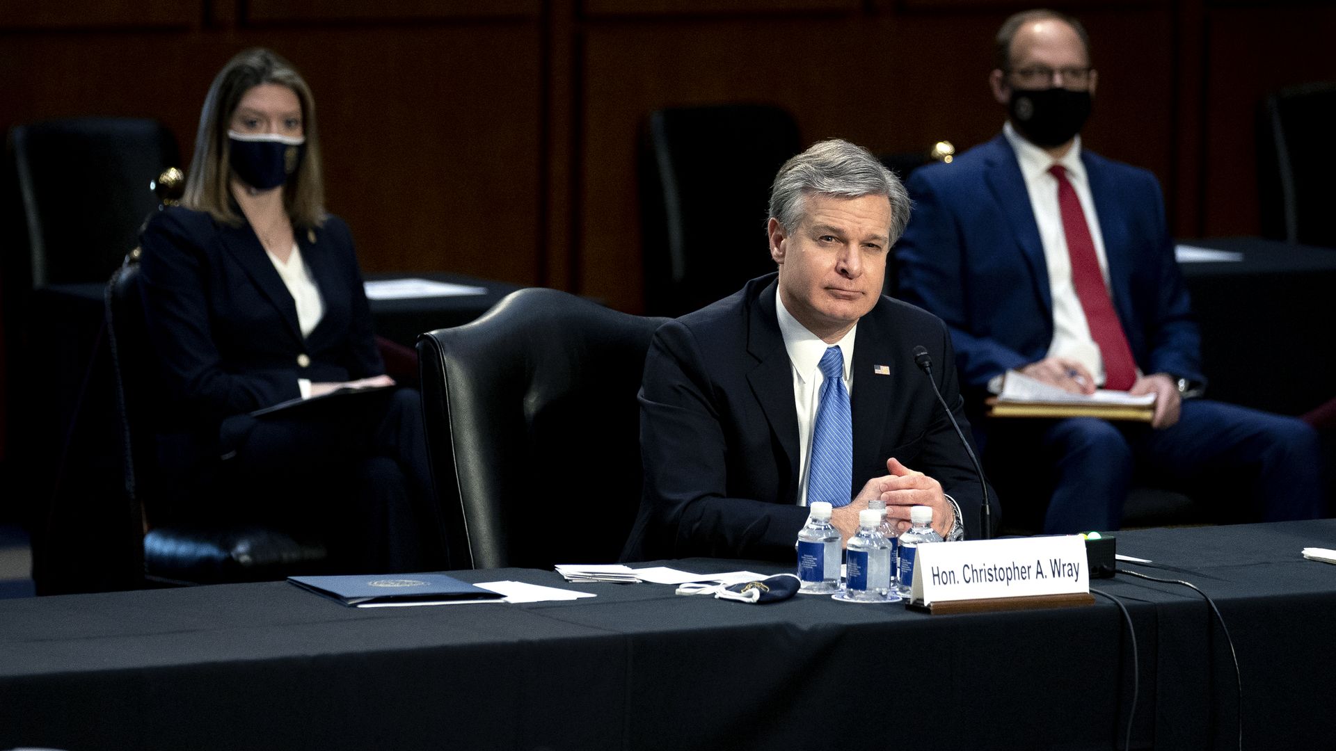 Photo of Christopher Wray sitting behind a desk with his hands folded